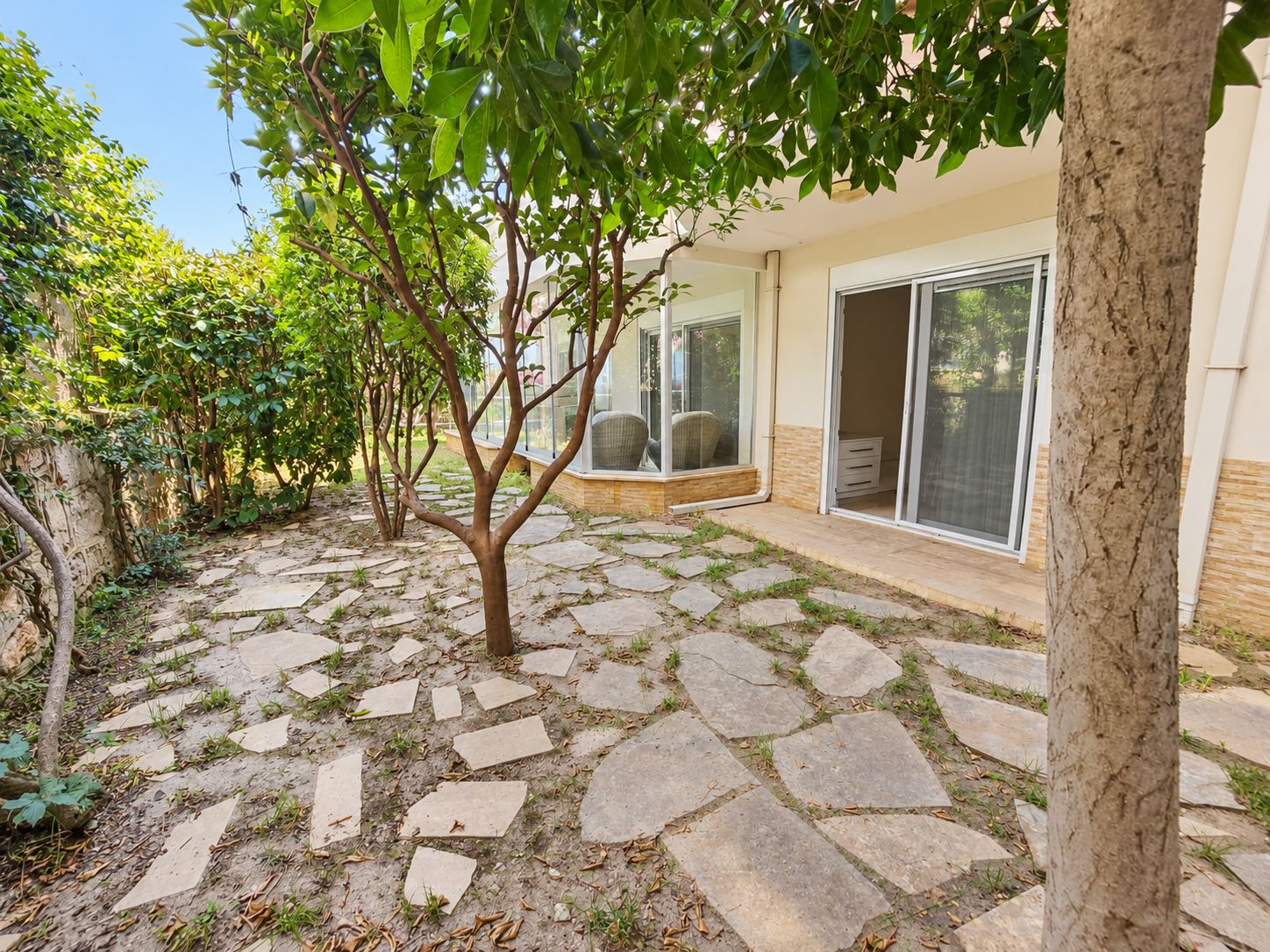 Garden with stone paving and dense shrubs beside a first-floor home for sale in Turkey