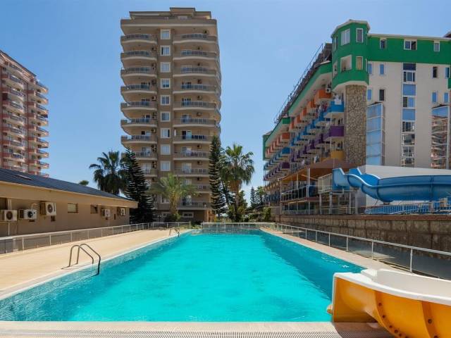 Бассейн с закрытой голубой горкой и пальмами в комплексе с апартаментами в Махмутларе, Турция