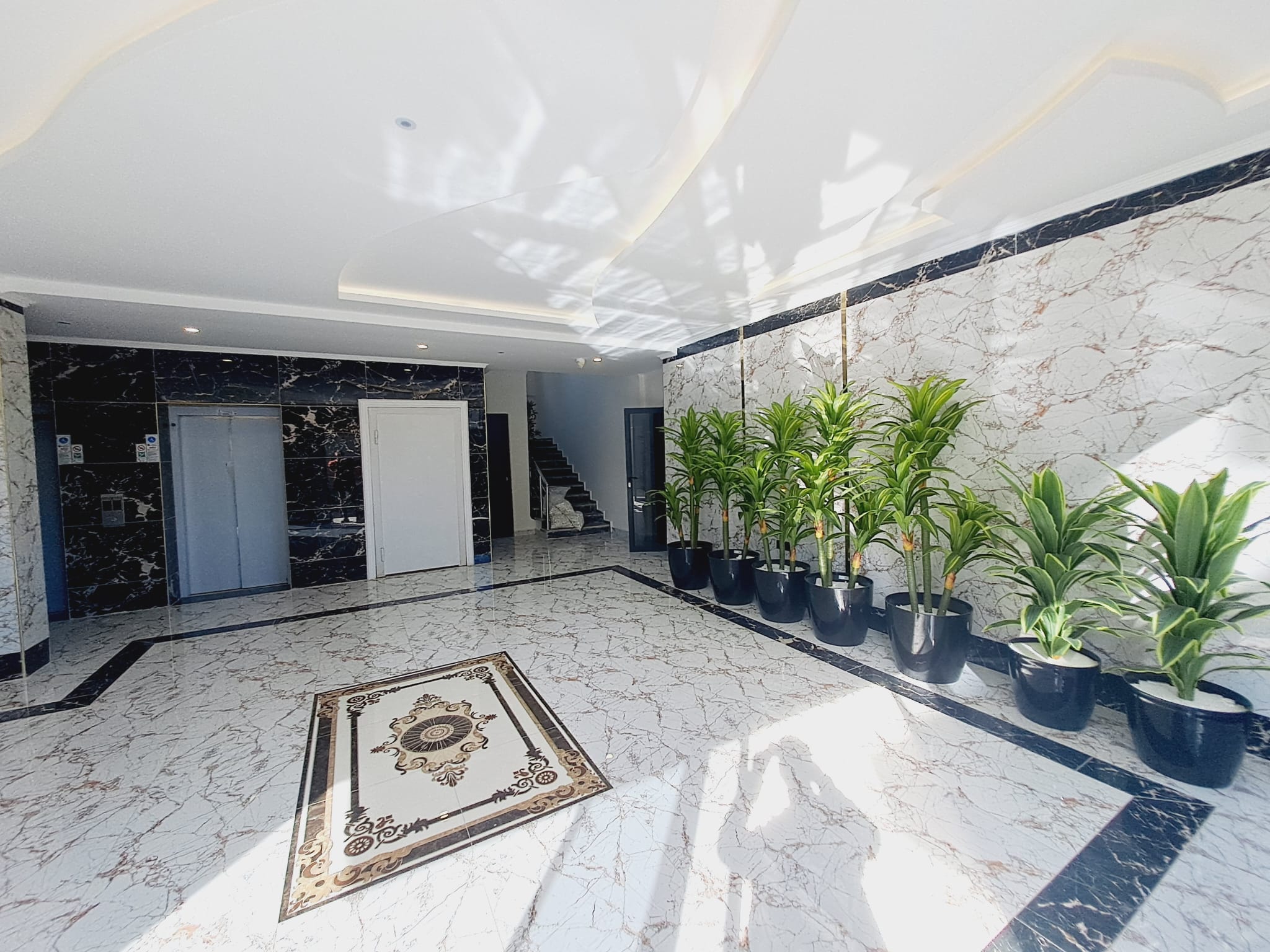 Светлое лобби с мраморной лифтовой зоной и зелёными растениями в комплексе с апартаментами 1+1 в продаже в Махмутларе