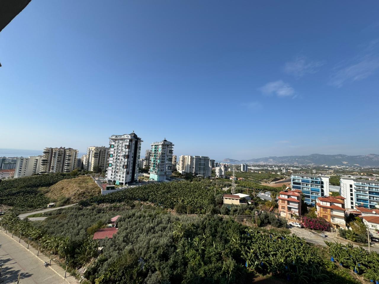 Панорама городской застройки, зелёных садов и горного хребта из квартиры