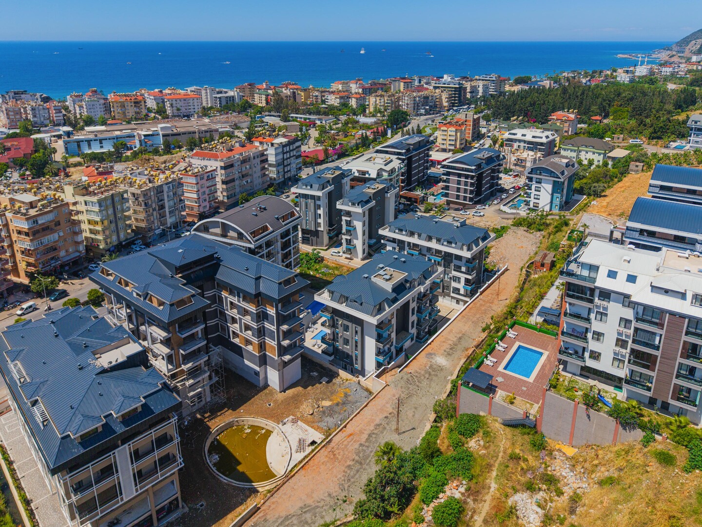 Панорама квартала с бассейном между корпусами и морем на горизонте для резиденции в Алании, Турция
