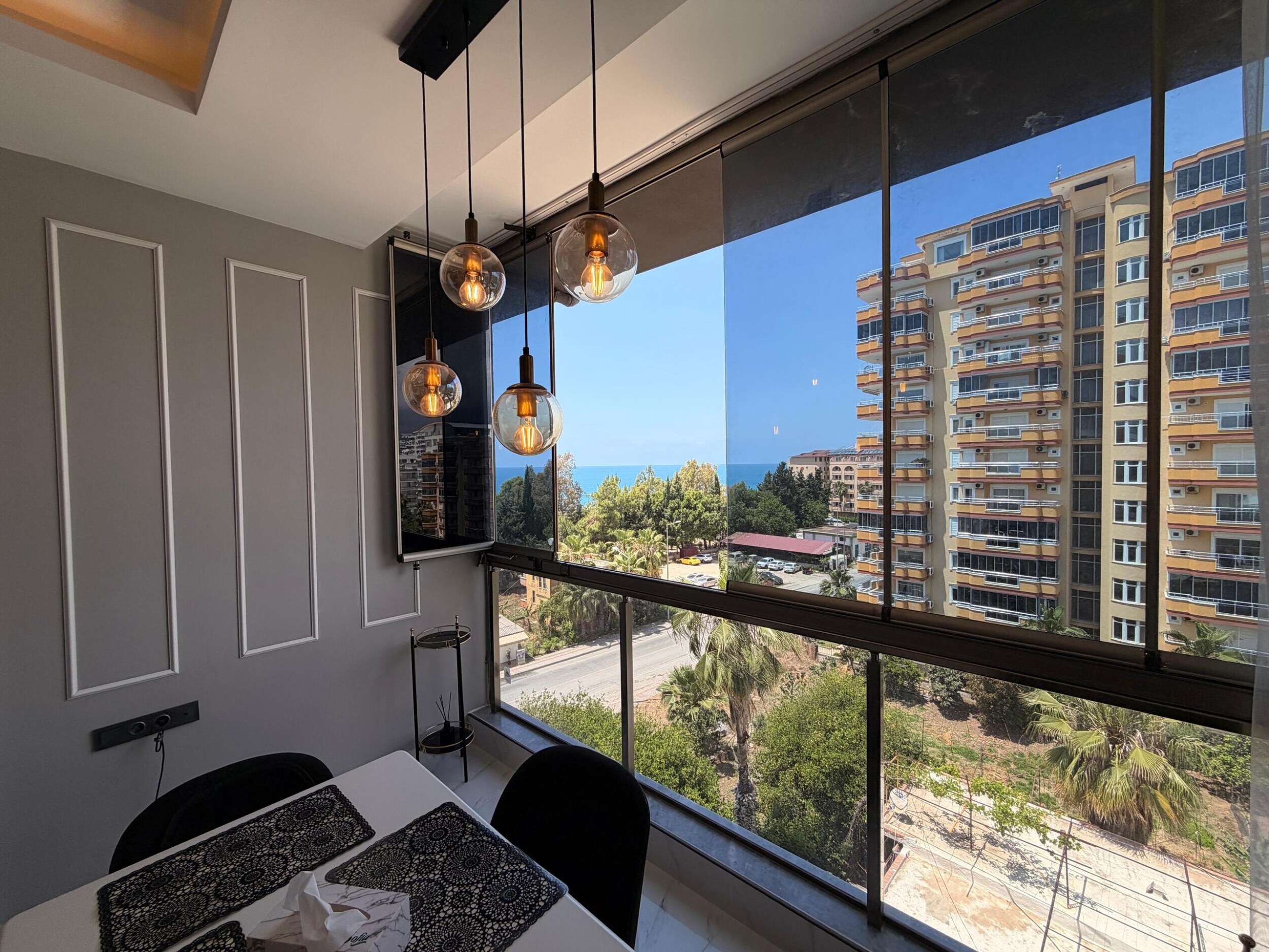 Kargıcak'taki penthouse yemek alanında beyaz masa, amber lambalar ve deniz manzarası