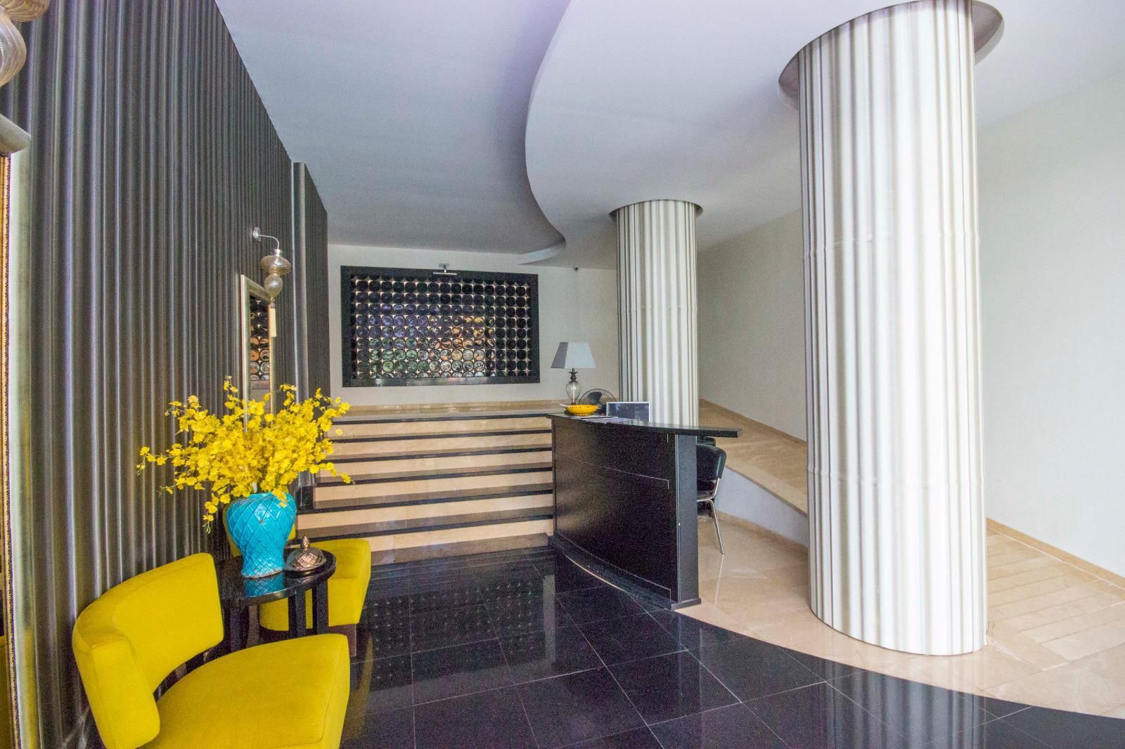 Lobide koyu resepsiyon bankosu, sarı koltuklar ve yivli sütunlar, satılık penthouseların bulunduğu komplekste