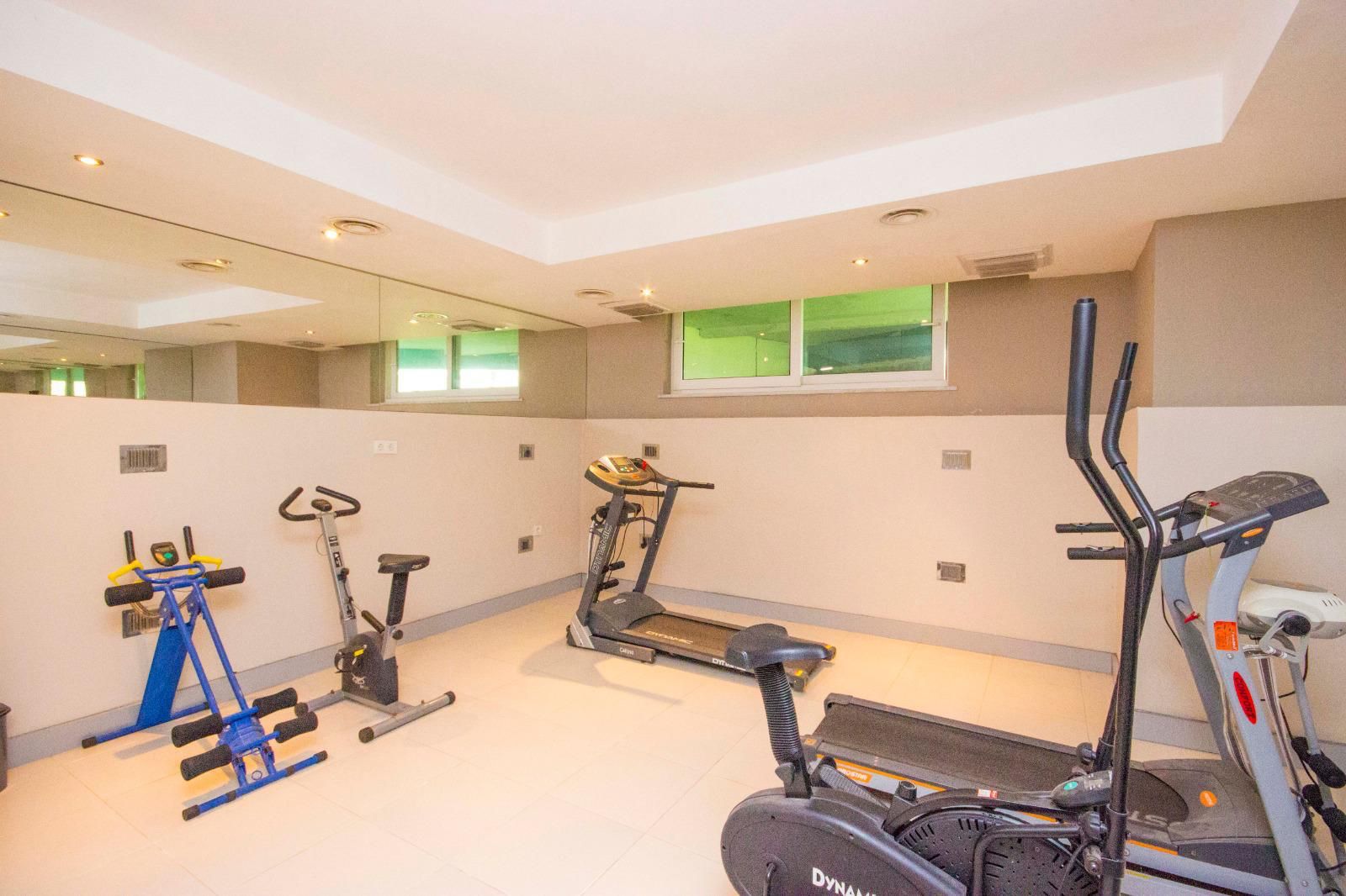Alanya’daki spor salonunda aynanın yanında kondisyon bisikleti, mavi ağırlık sehpası ve alçak pencere
