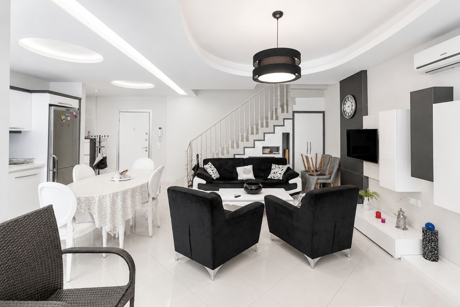 Siyah kanepe, beyaz mutfak ve beyaz korkuluklu merdivenli mutfaklı salon, satılık konutta