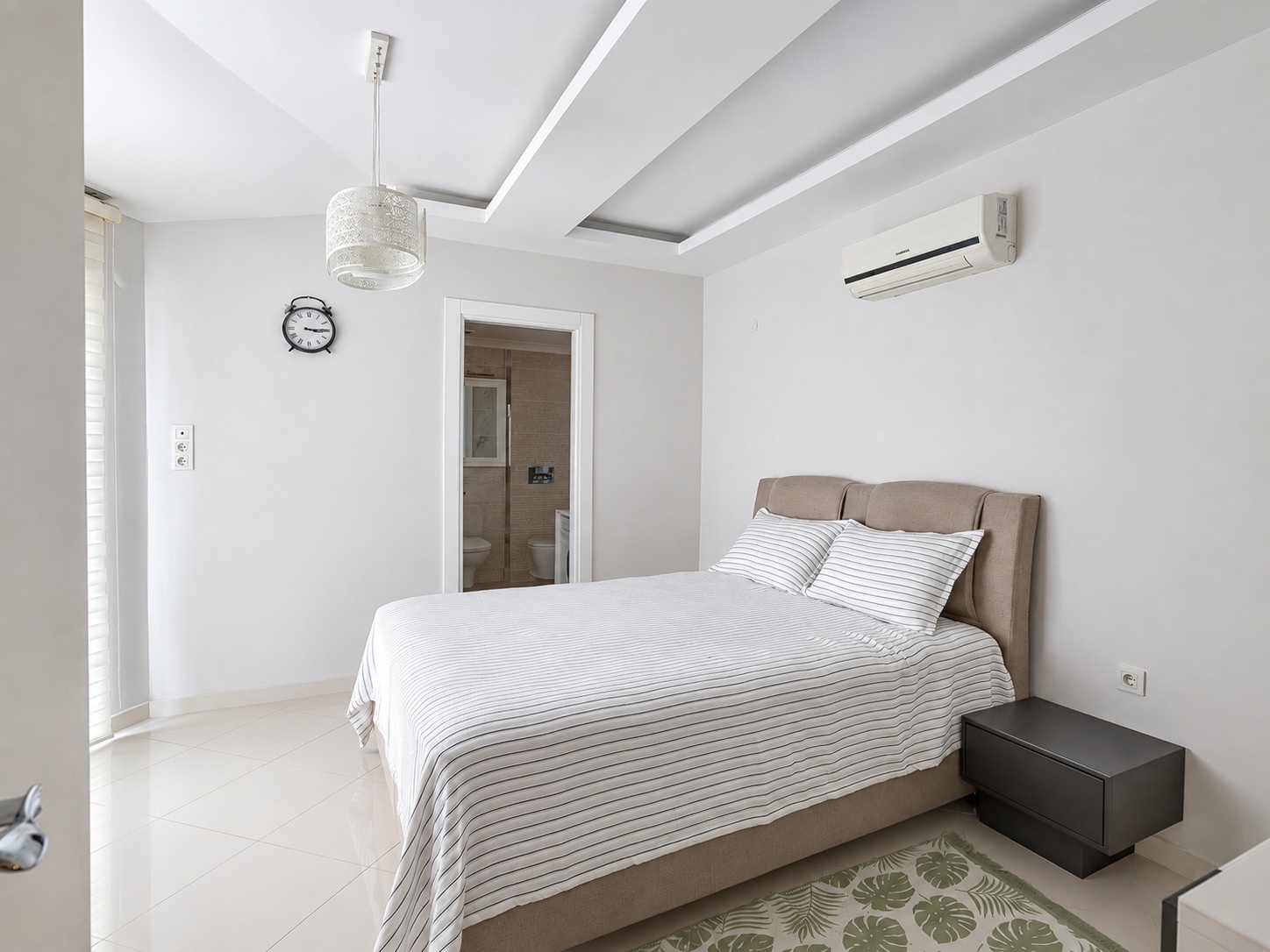 Yatak odasında bej yumuşak başlıklı çift kişilik yatak, çizgili örtü ve banyo kapısı, penthouse’da