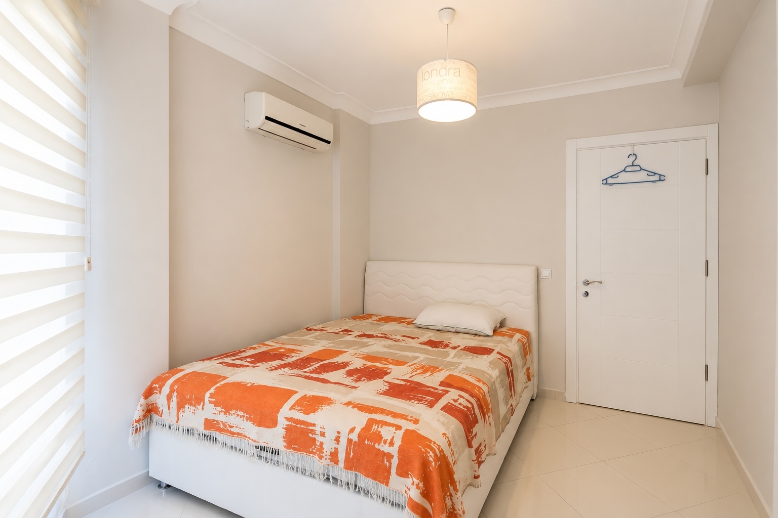 Turuncu beyaz geometrik örtülü yatak, çizgili stor perde ve kumaş abajurlu yatak odası, 3+1 penthouse’da