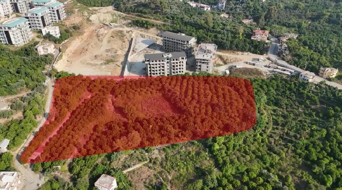 Havadan kırmızı sınırla işaretli arazide inşaat blokları ve kıvrımlı ulaşım yolu, satılık konutlar yanında