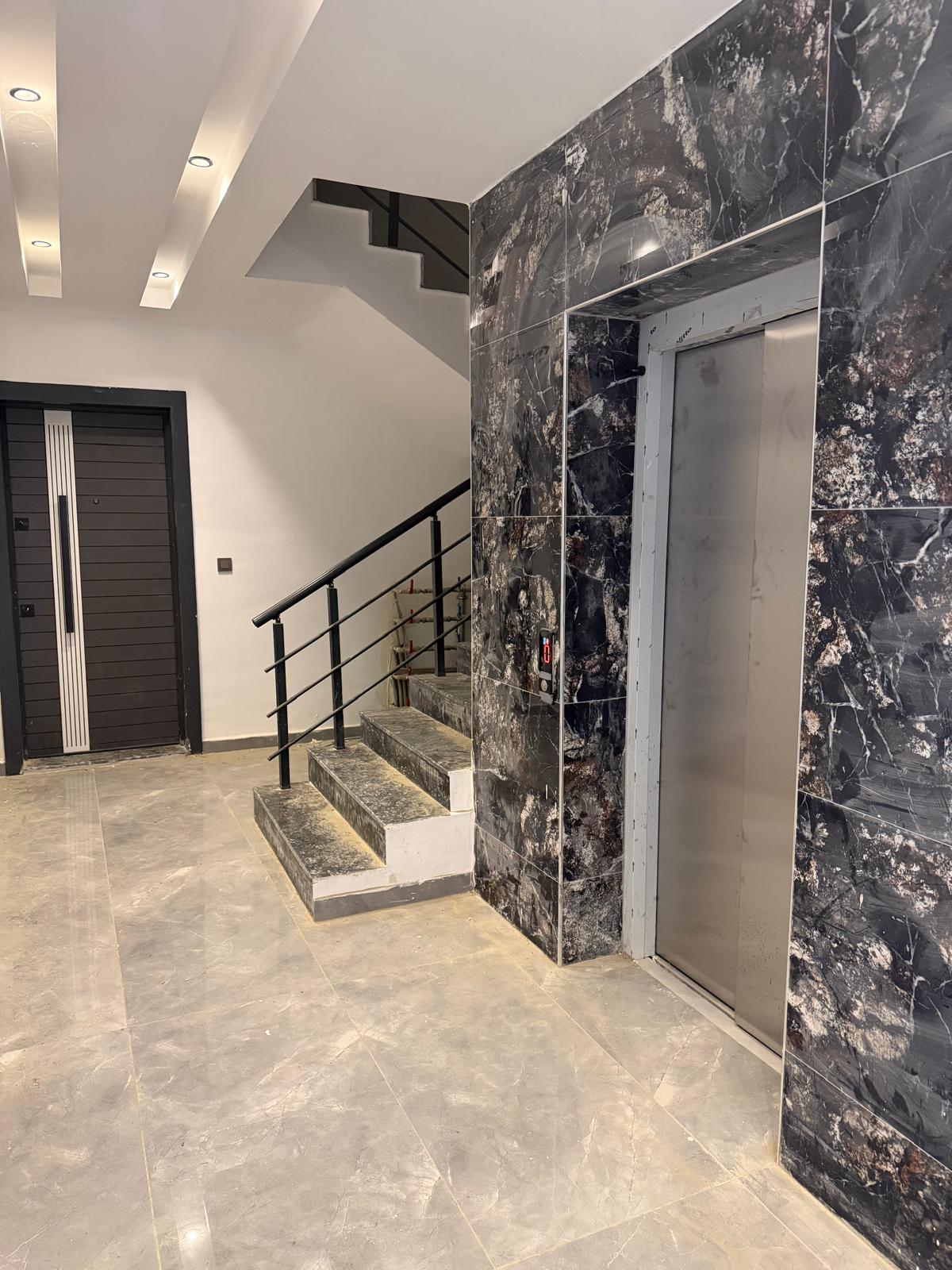 Lobby with a dark marble lift door and light marble flooring in a complex with apartments for sale in Turkey