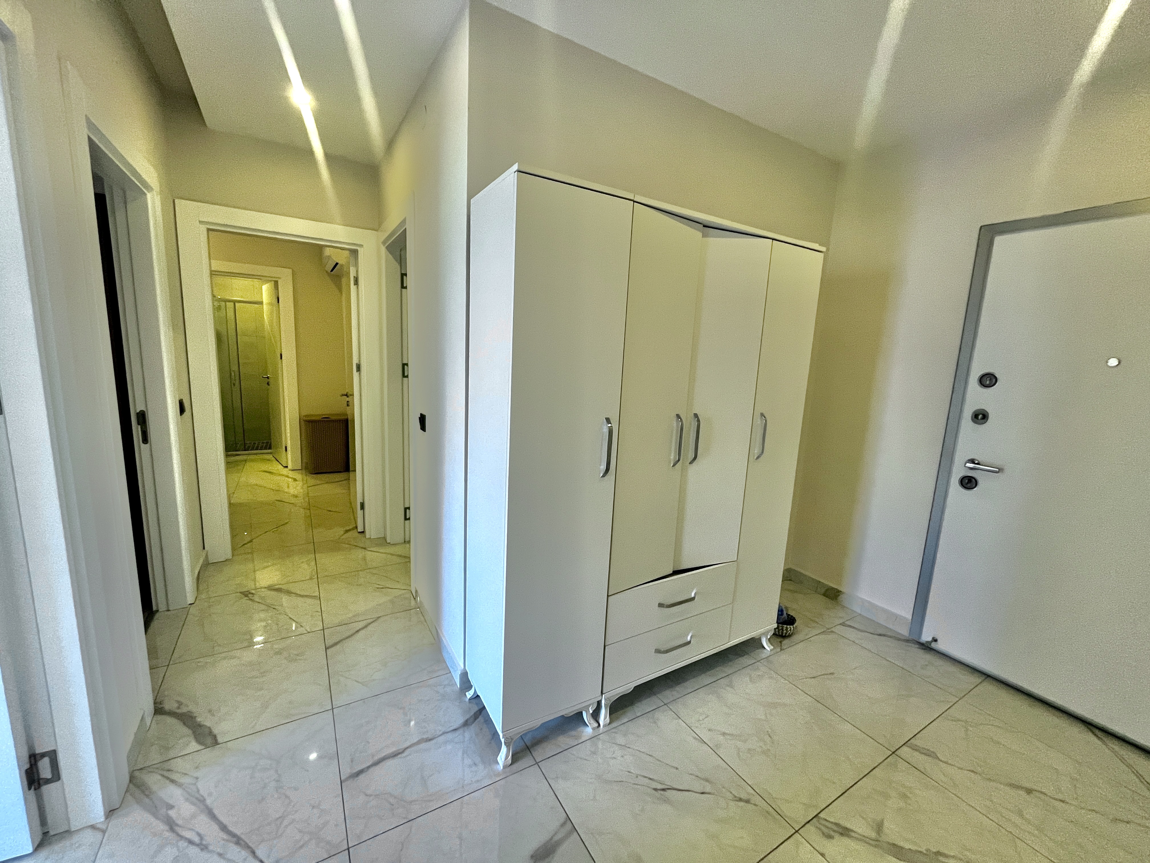 Entry hall with white cabinet, mirrored door and marble tile in an apartment in Alanya