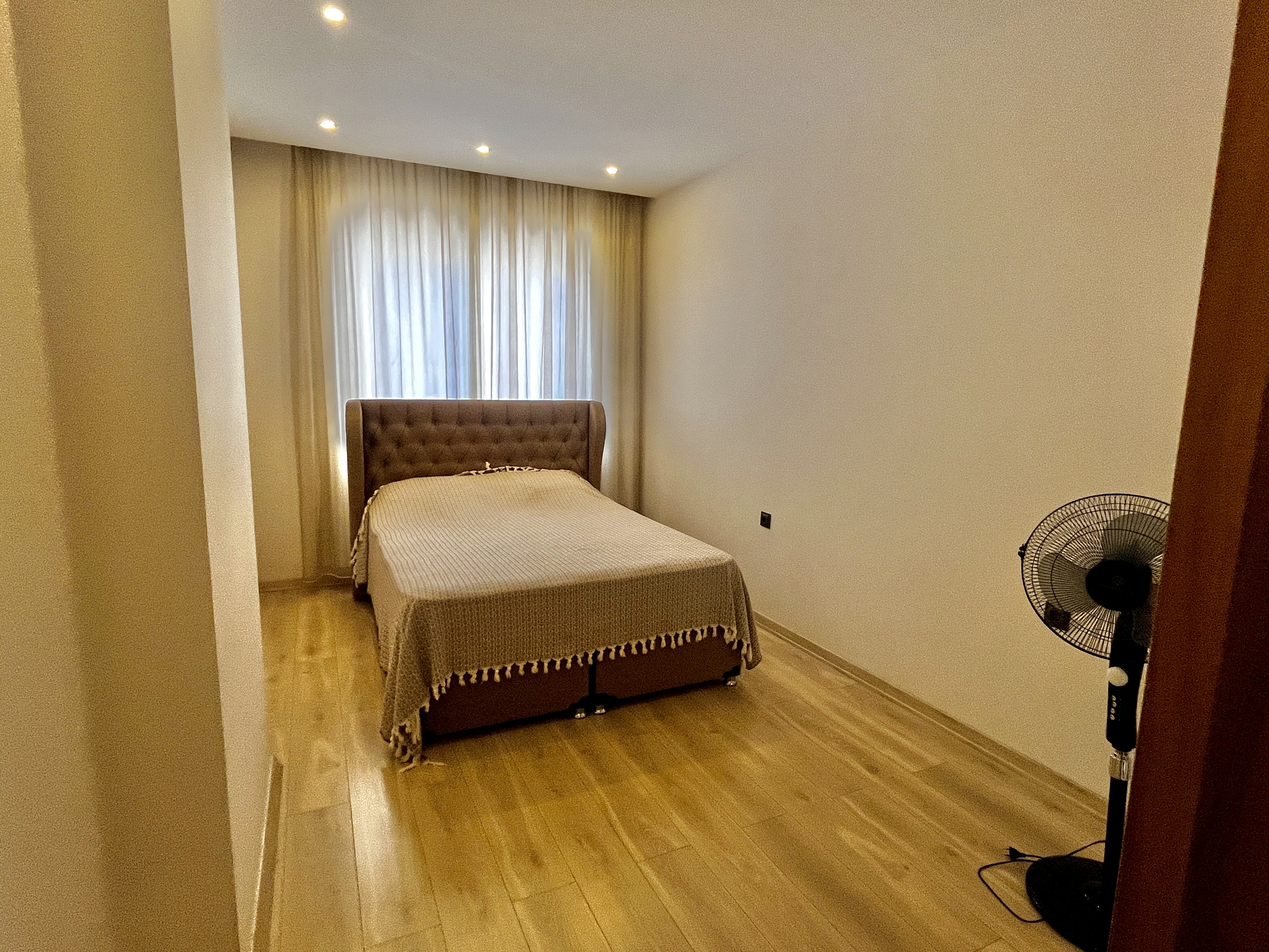 Bedroom with double bed, brown headboard and curtained window in Alanya