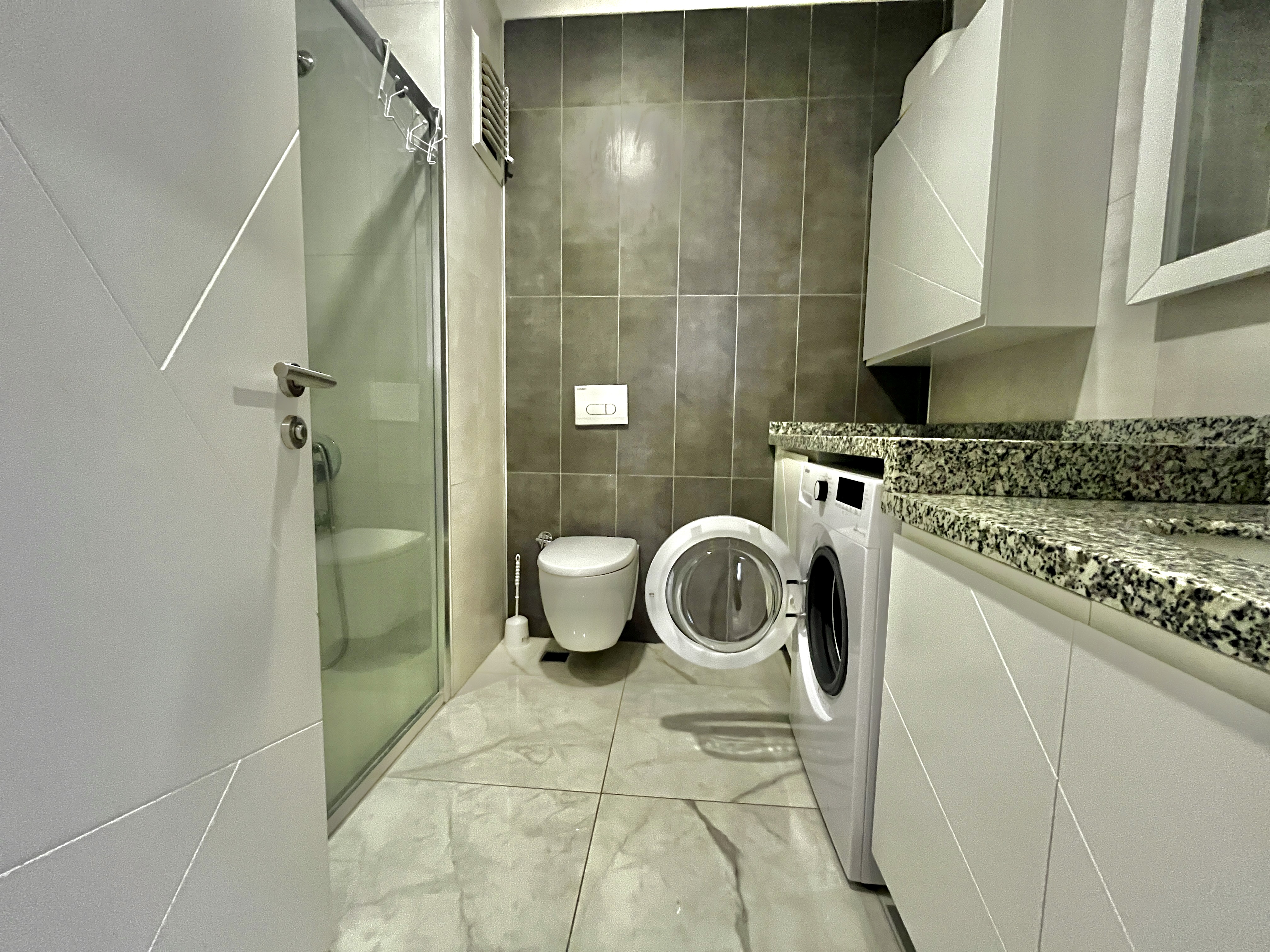 Bathroom with glass shower, washing machine and marble tile in an apartment in Alanya