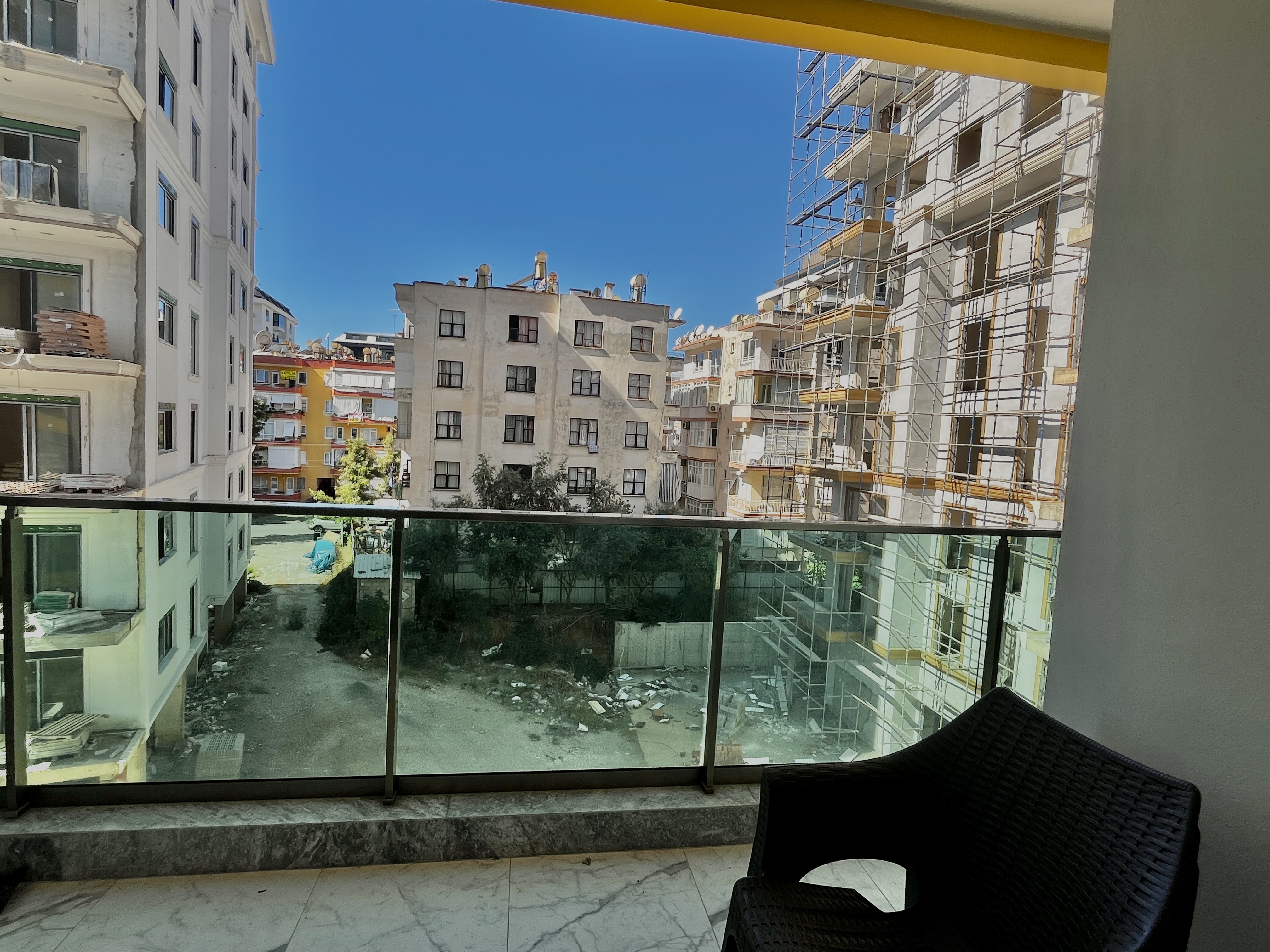 Balcony with glass railing, wicker chair and views of residential buildings from an apartment