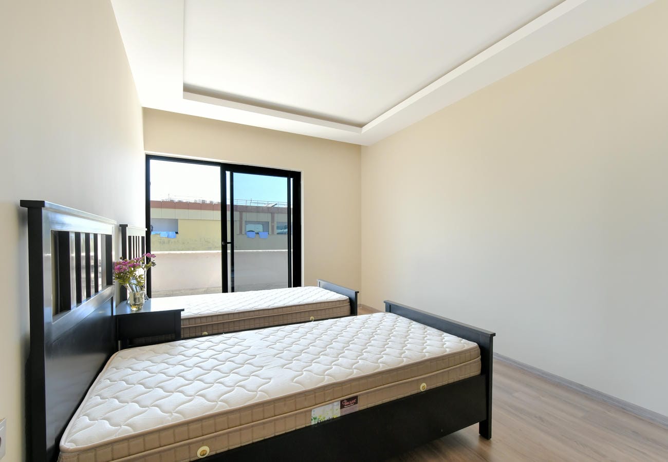 Alanya’da yatak odasında iki tek kişilik yatak ve balkon çıkışlı sürgülü cam kapı