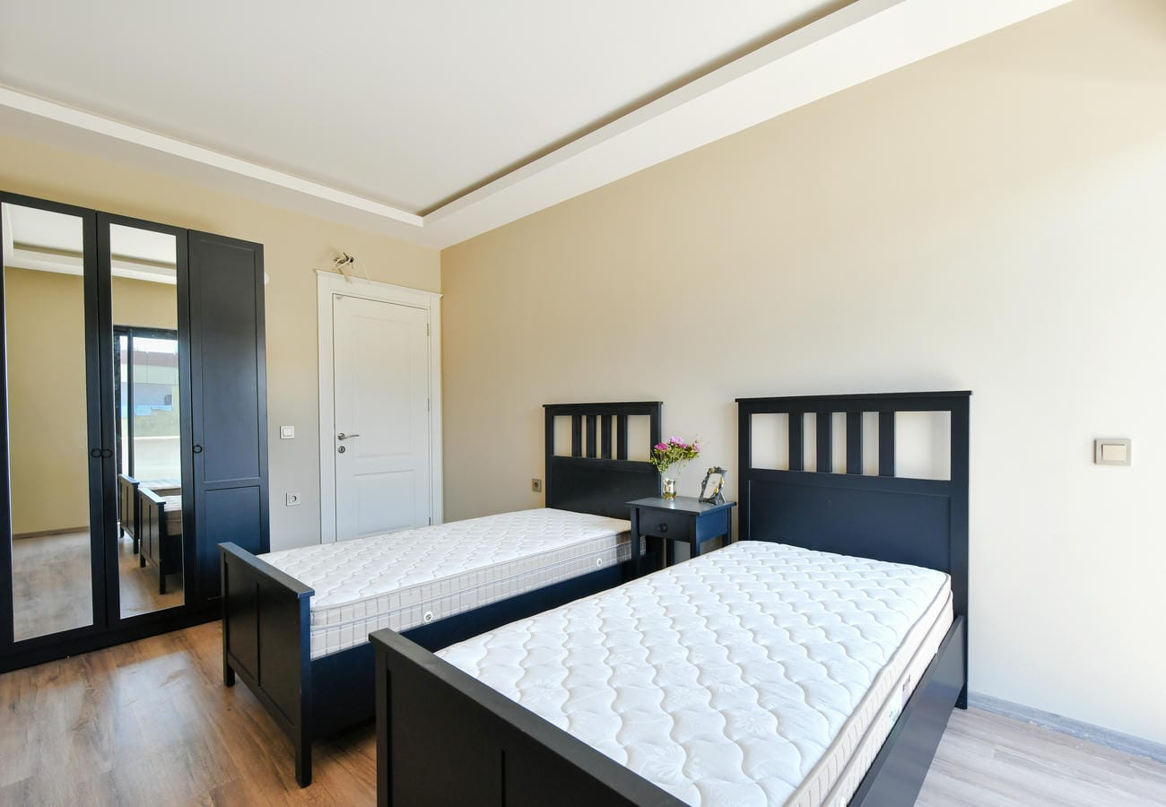 Penthouse yatak odasında iki tek kişilik yatak, koyu gardırop ve siyah komodin