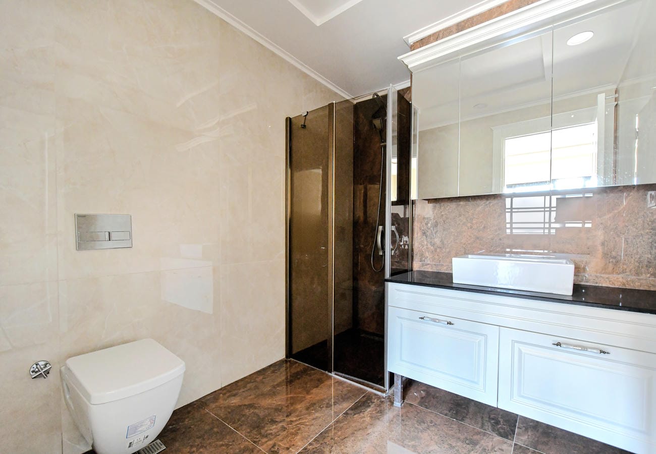 Penthouse banyosunda cam duş bölmesi, çanak lavabo ve koyu kahverengi fayanslar