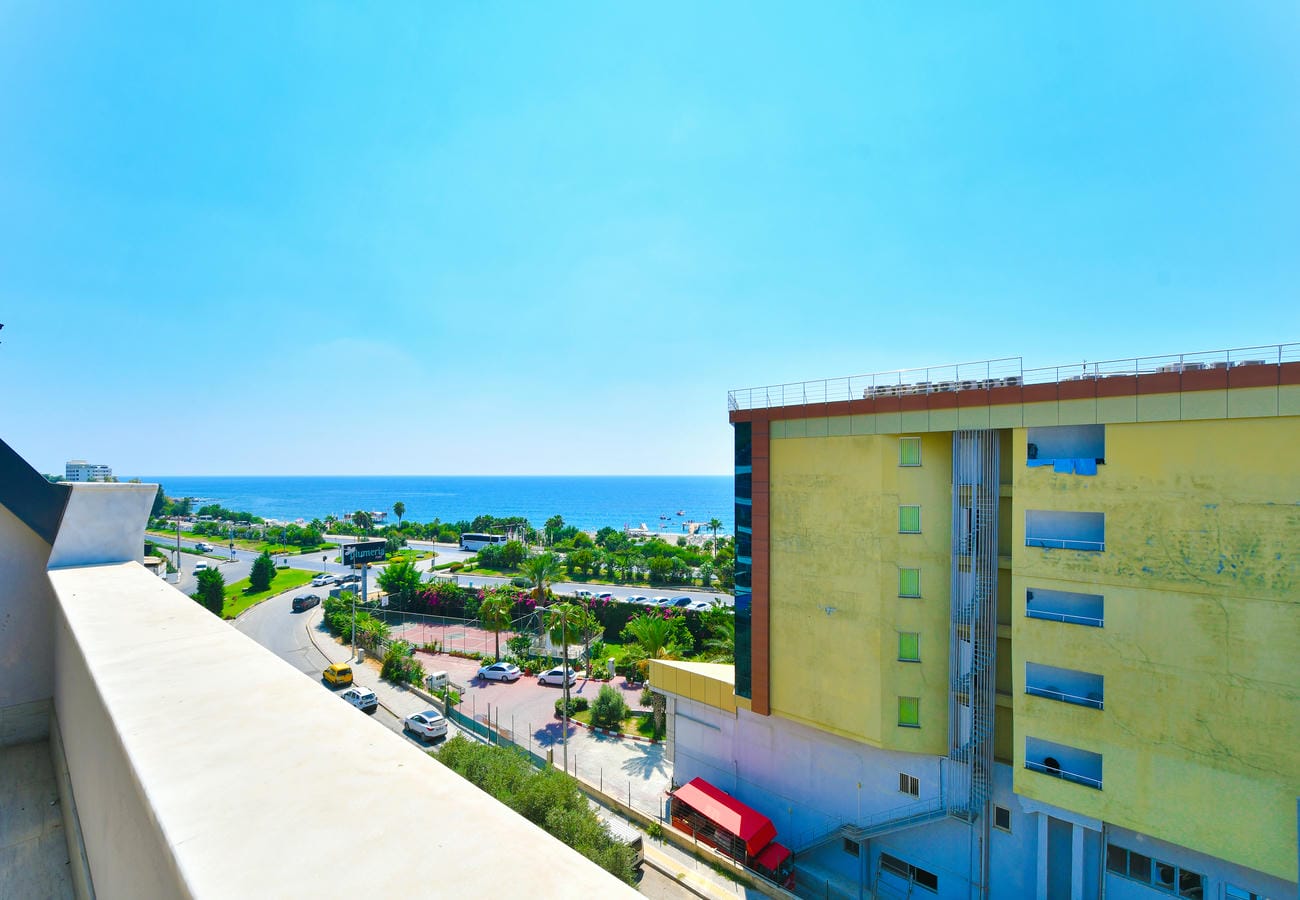 Penthouse terasından mavi denize, kıyıdaki yeşilliğe ve araçlı şehir yoluna bakış