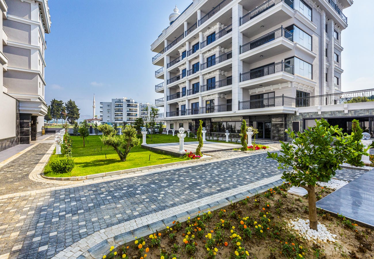 Daireli sitenin çiçeklik ve genç ağaçlarla çevrili taş döşeli giriş yolu