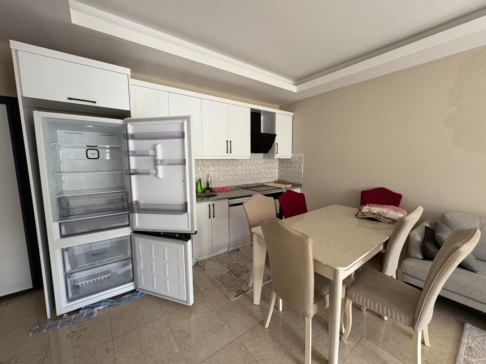 Beyaz dolaplı, siyah davlumbazlı ve dört sandalyeli mutfak, Alanya’daki dairede