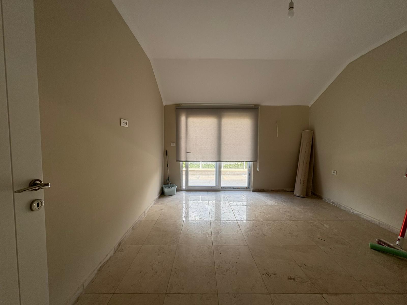 Bej duvarlı, balkon kapılı ve stor perdesi inik boş yatak odası, dairede