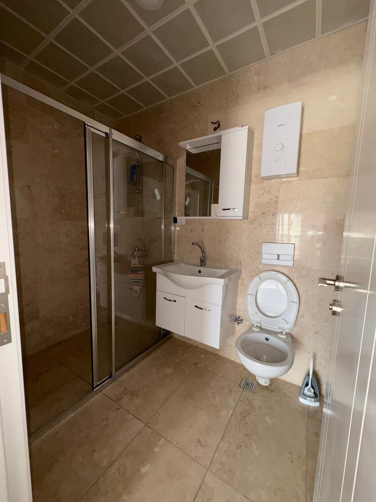 Sürgülü cam duş kabinli ve bej mermer kaplamalı banyo, dairede