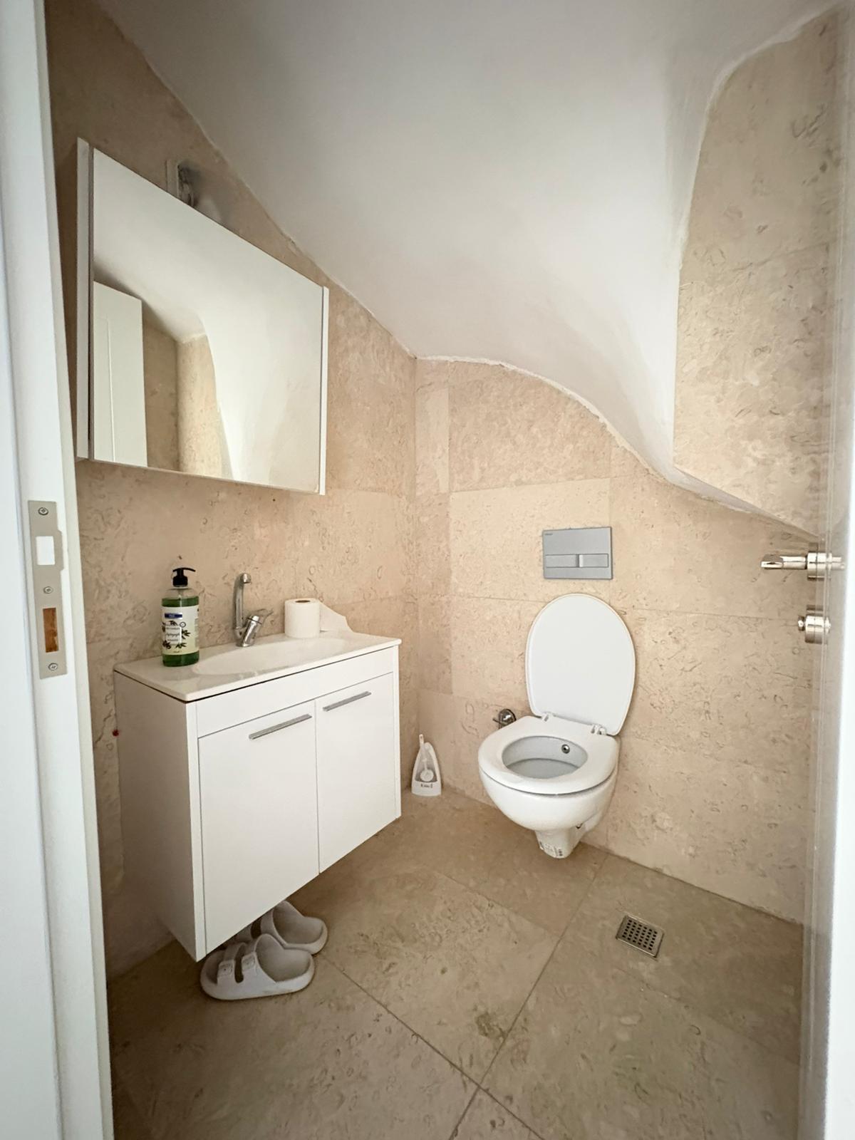 Bej mermer duvarlı, aynalı dolaplı ve asma klozetli banyo, Alanya’daki 3+1 rezidansta