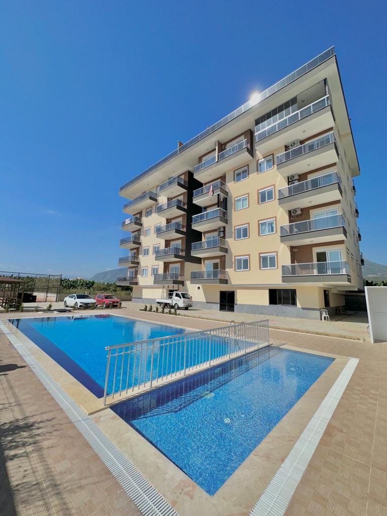 Gündüz mavi sulu açık havuz, Alanya’daki dairelerin bulunduğu kompleksin önünde