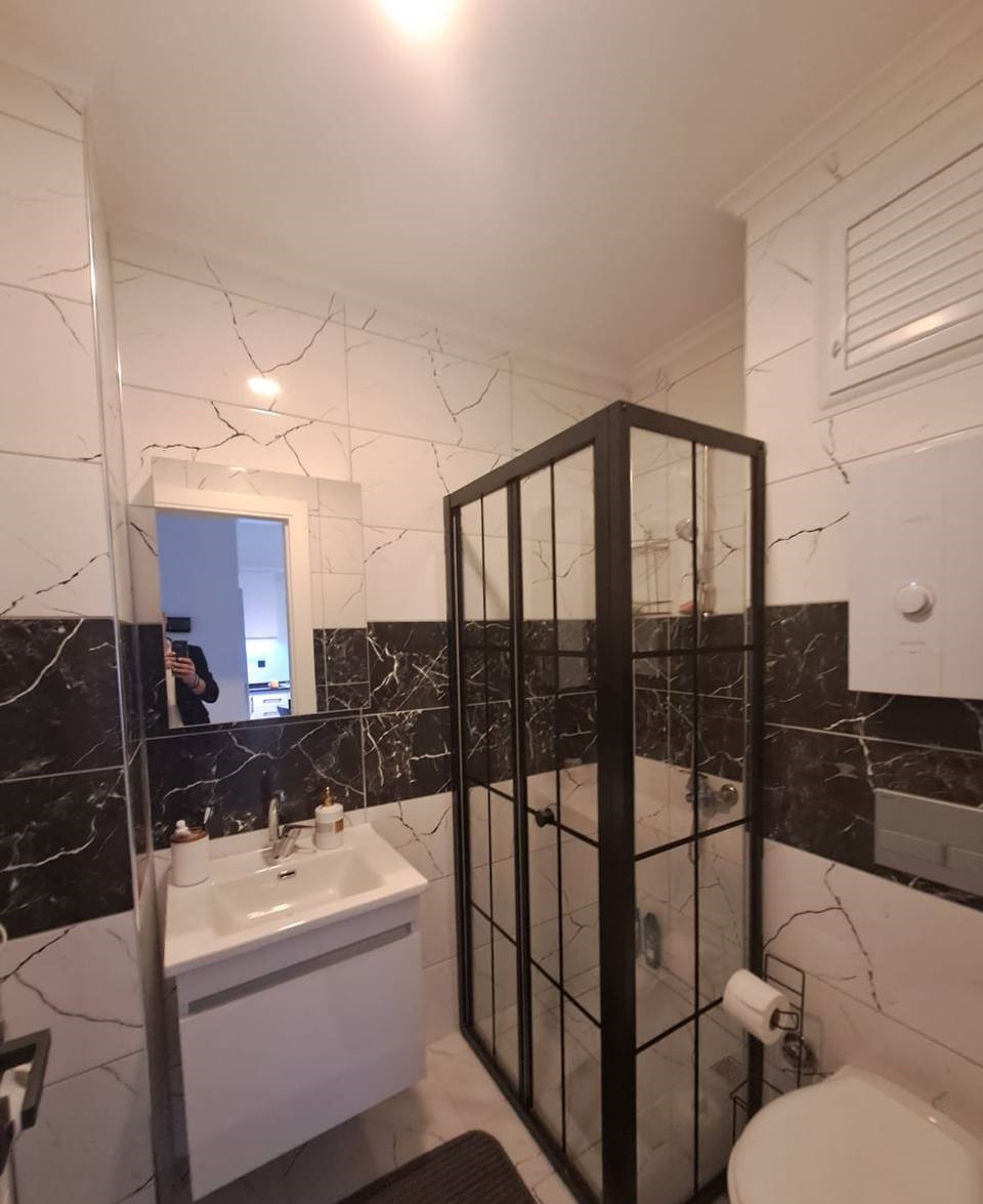 Cam duş kabinli banyo, Avsallar’da konutta beyaz lavabo dolabı ve duvardaki aynayla