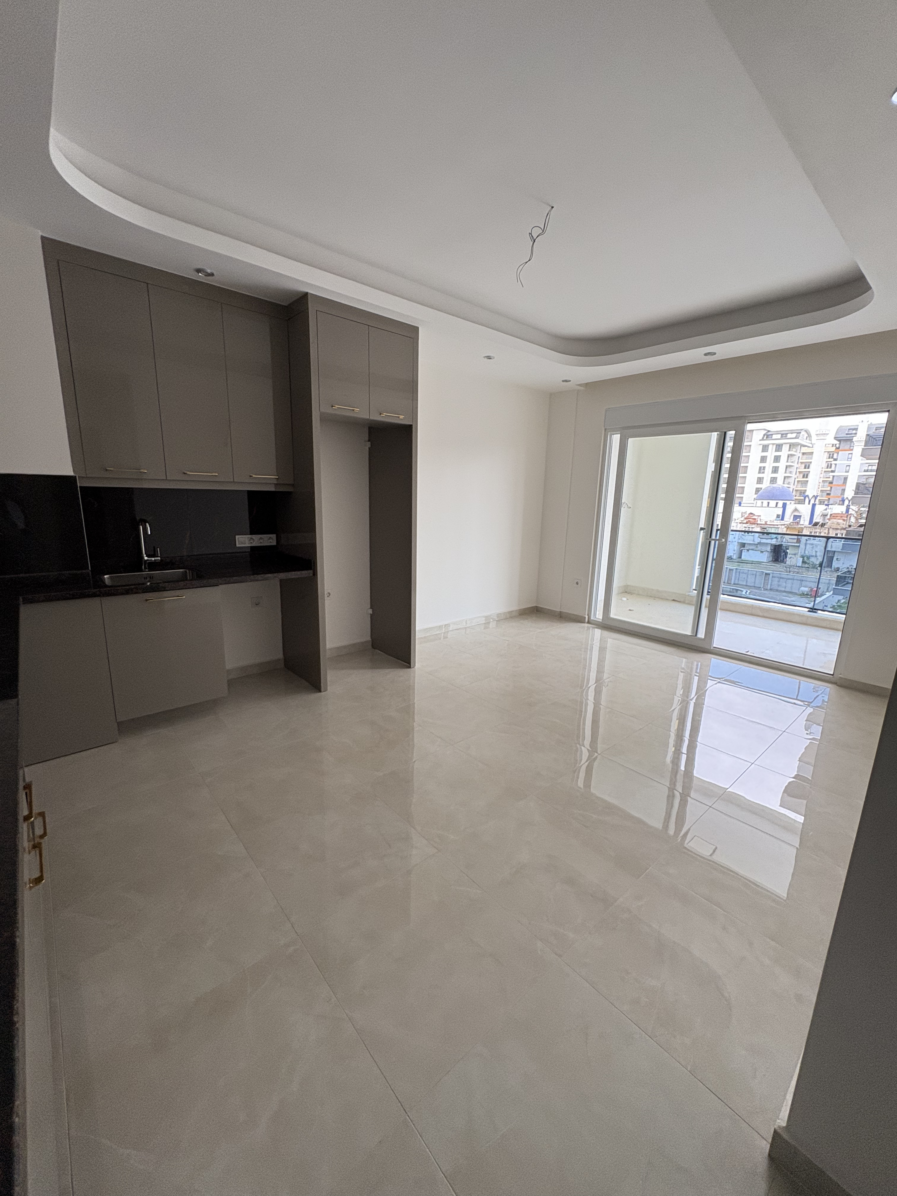Gri ankastreli mutfaklı salon, satılık dairede balkona açılan sürgülü pencereyle