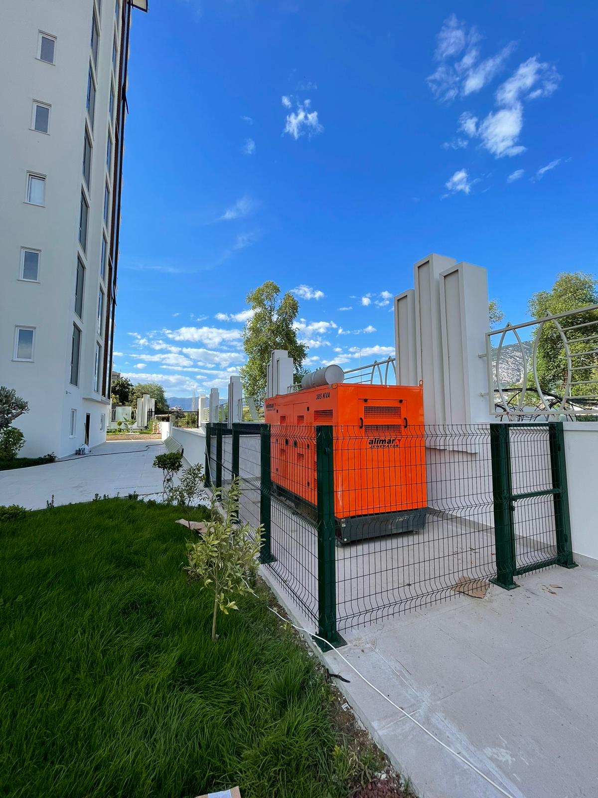 Metal çitli turuncu jeneratör, Mahmutlar’daki dairelerin bulunduğu rezidansın yanında