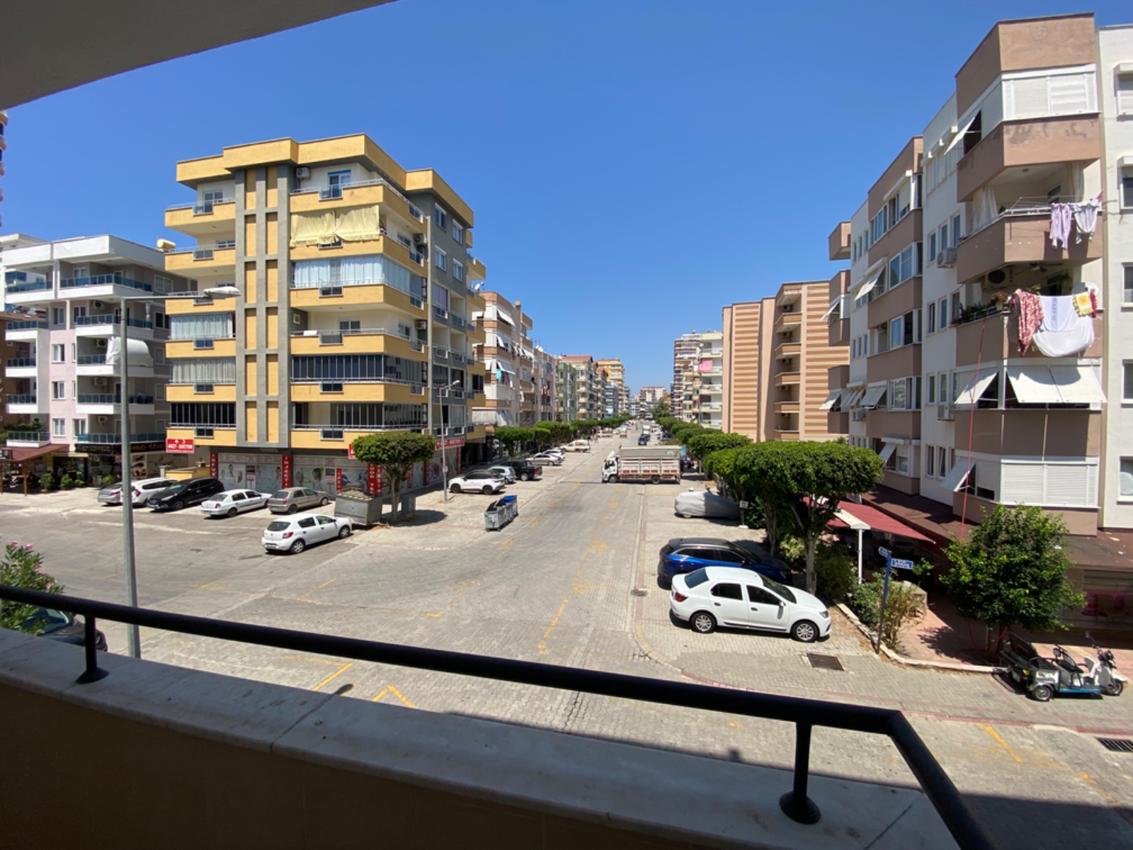 Türkiye’deki konut balkonunda siyah metal korkuluklar, şehir sokağı ve park edilmiş araçlar görülüyor