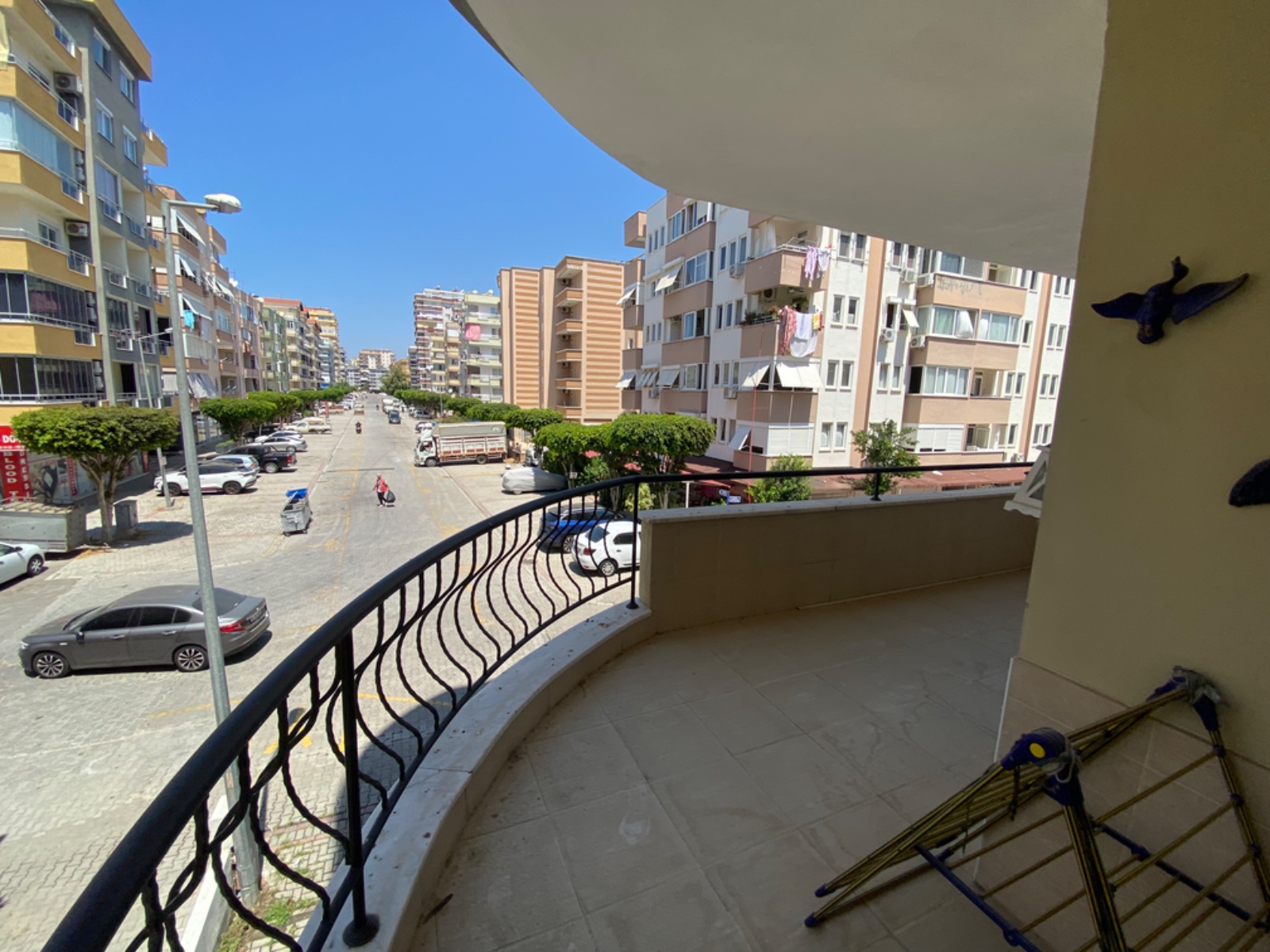 Mahmutlar’da satılık konutun balkonundan şehir caddesi, araçlar ve çevredeki yüksek binalar izleniyor