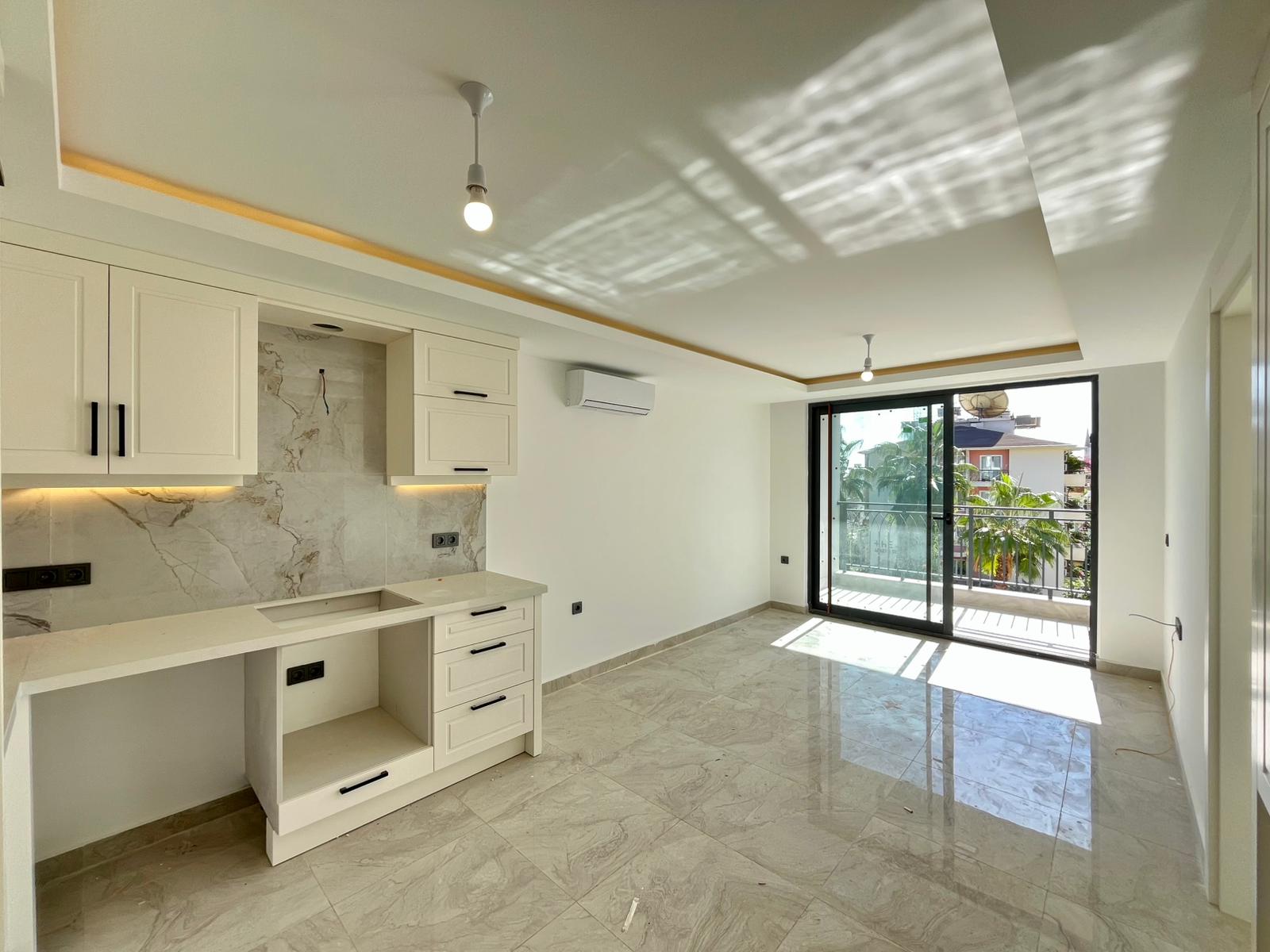 Built-in kitchen-living room with white cabinets and a balcony door in a flat in Alanya
