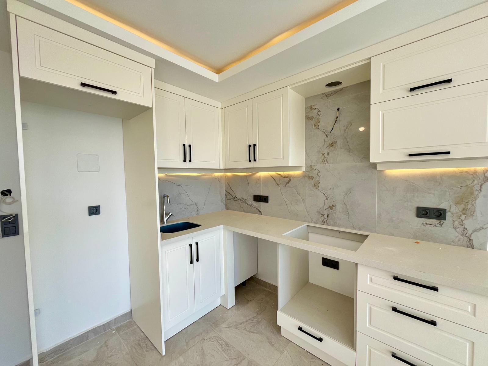White corner kitchen with a marble countertop, patterned backsplash and built-in upper cabinets