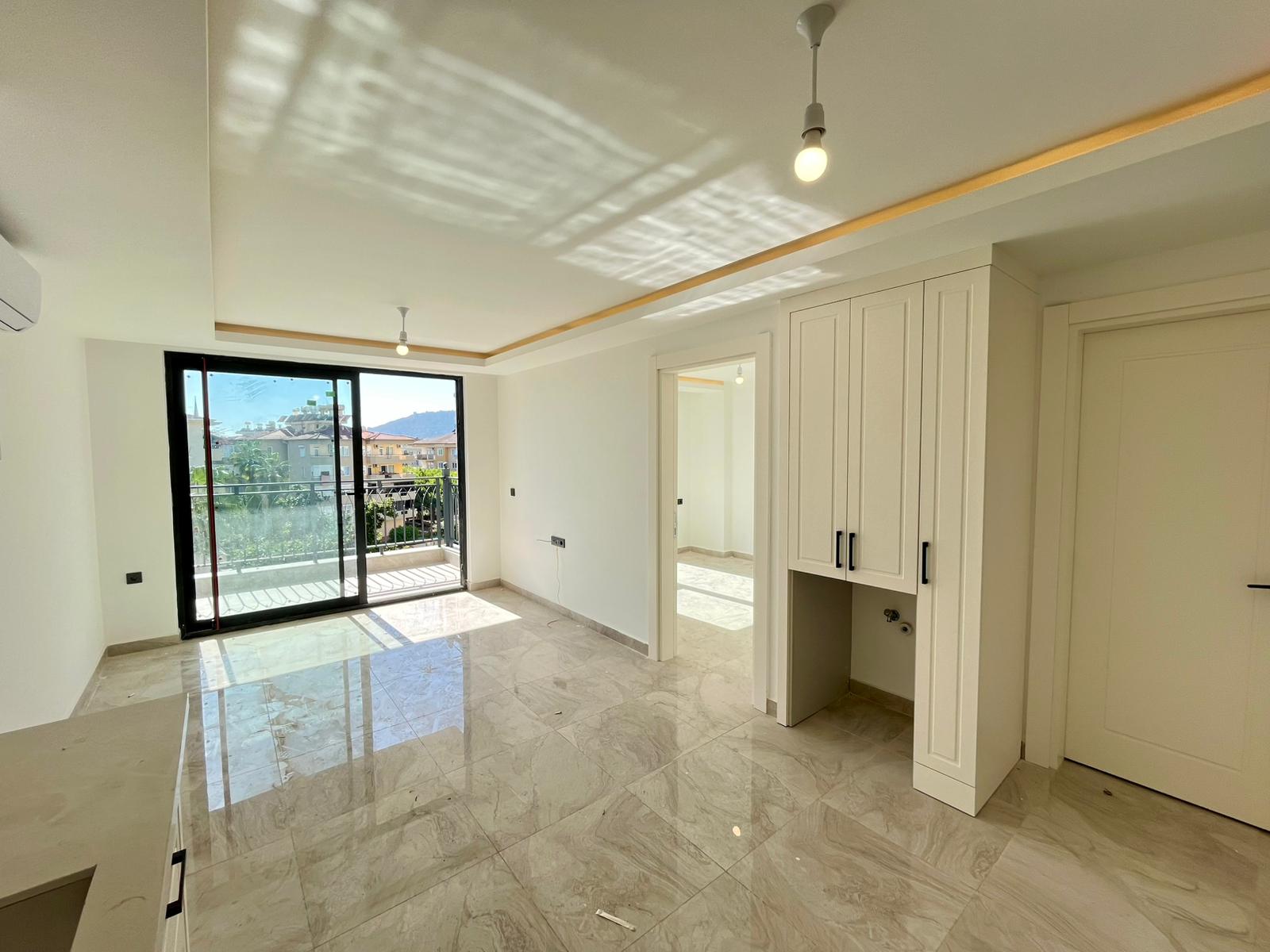 Empty kitchen-living room with marble floor and balcony access in a residence for sale in Turkey