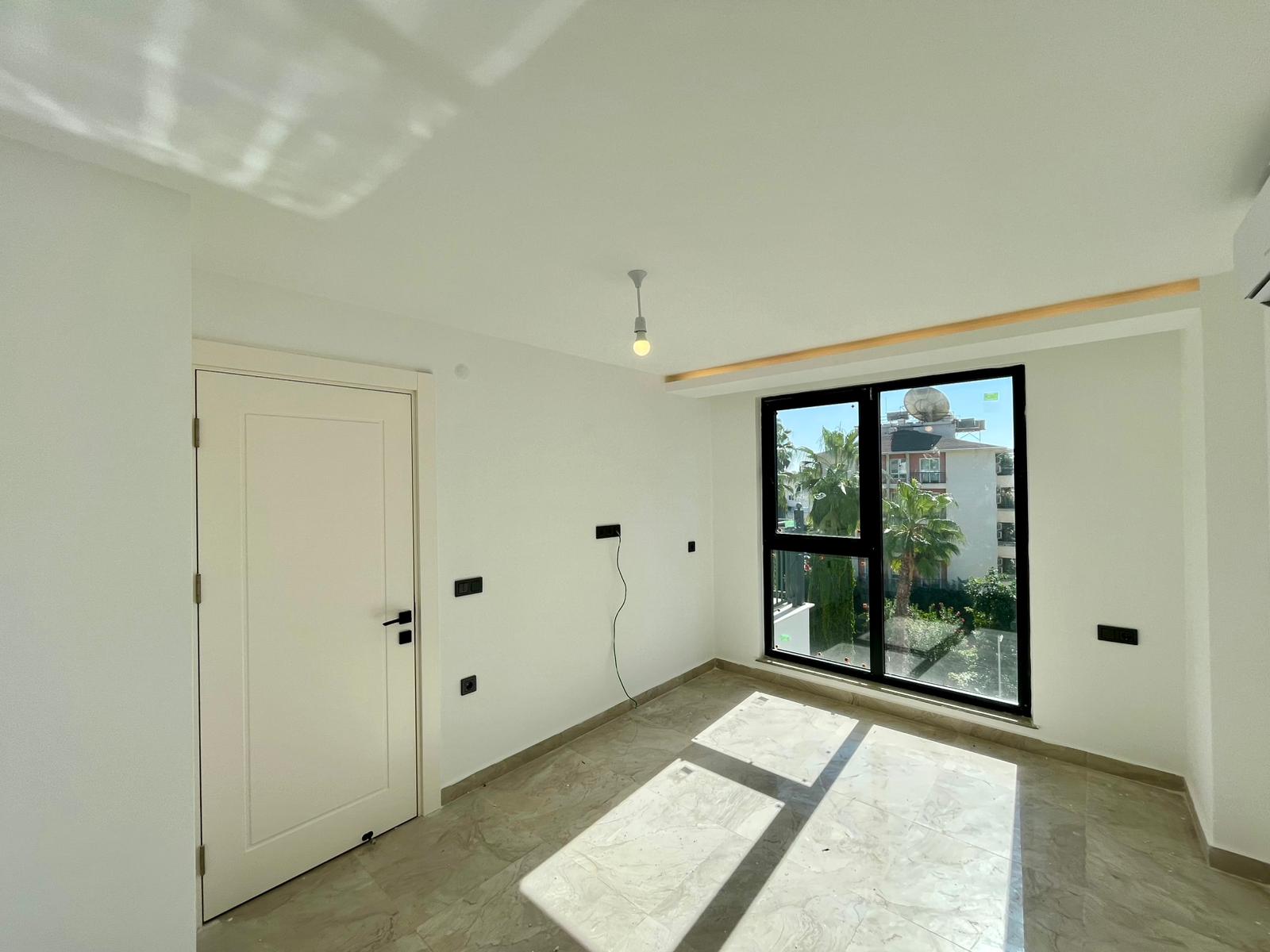 Sunlit bedroom with a panoramic black-framed window and marble-effect floor in Alanya