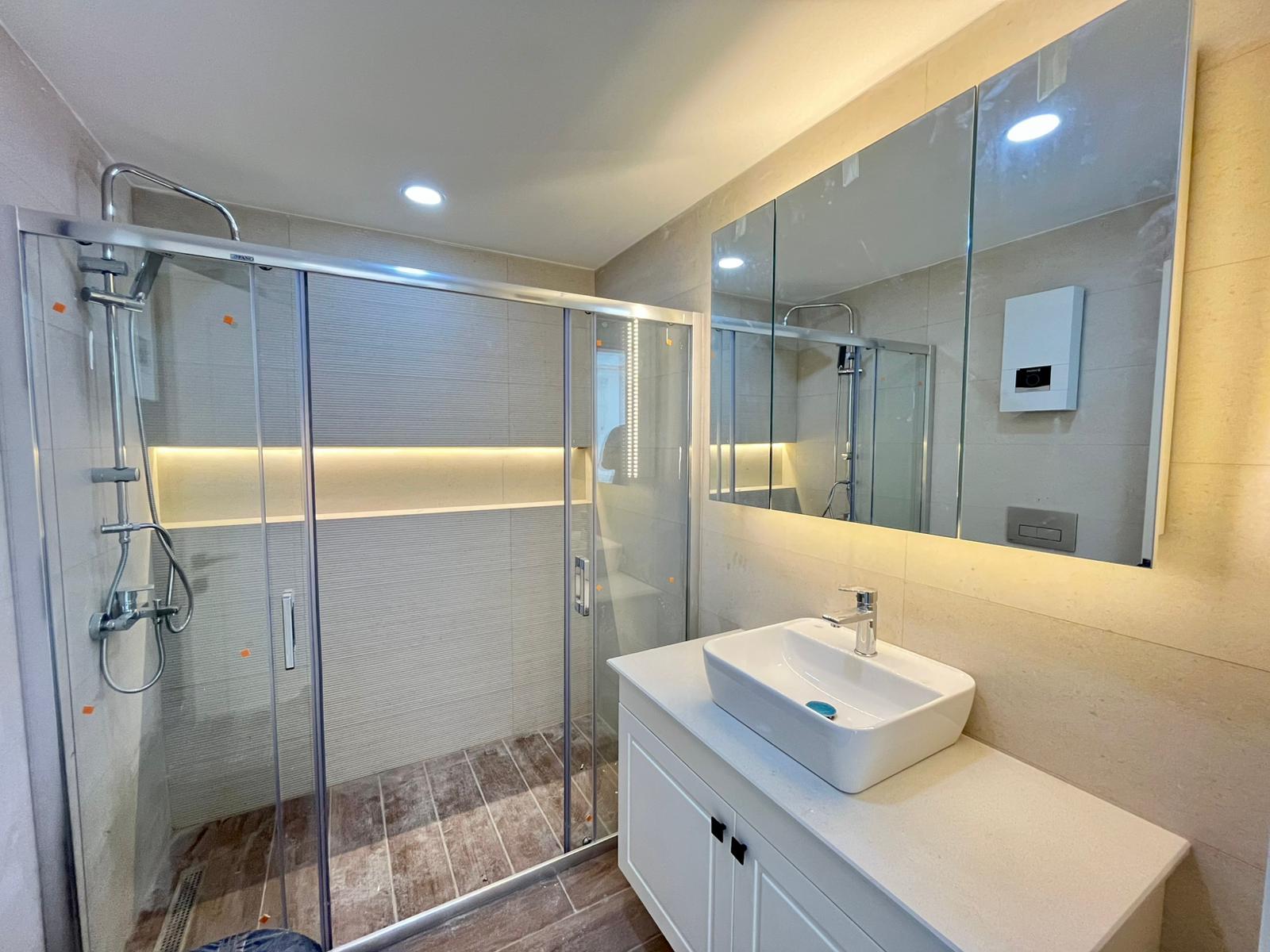 Bathroom with a glass shower enclosure, white basin and large mirrored panel in a home