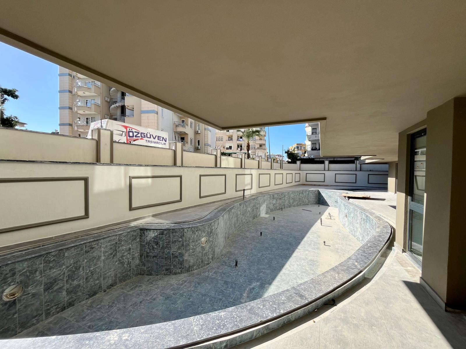 Unfinished curved pool with marble-effect edging and panoramic glazing in a complex with apartments in Turkey