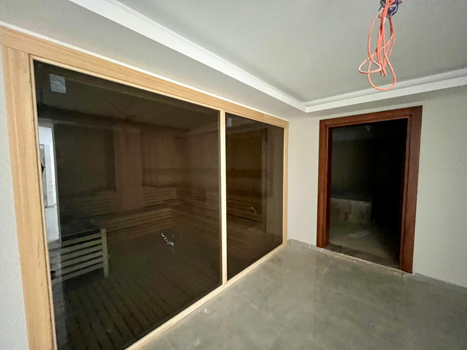 Sauna with a glass door, wooden lining and shelves in a complex with apartments