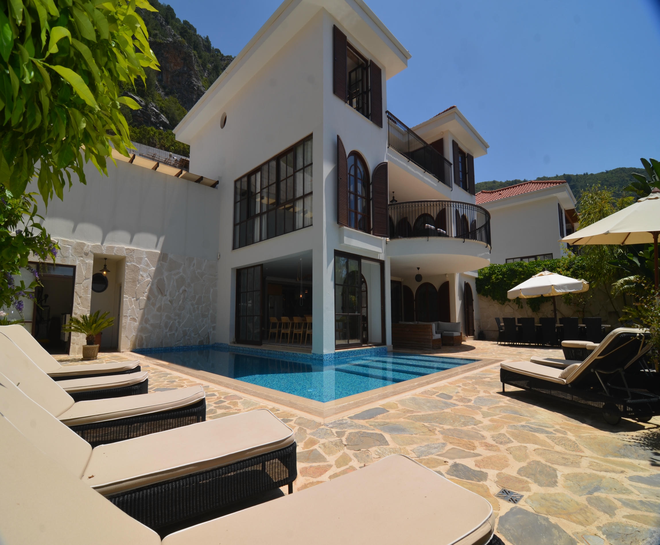 Blue mosaic pool beside a white villa with panoramic windows and loungers in Turkey for sale