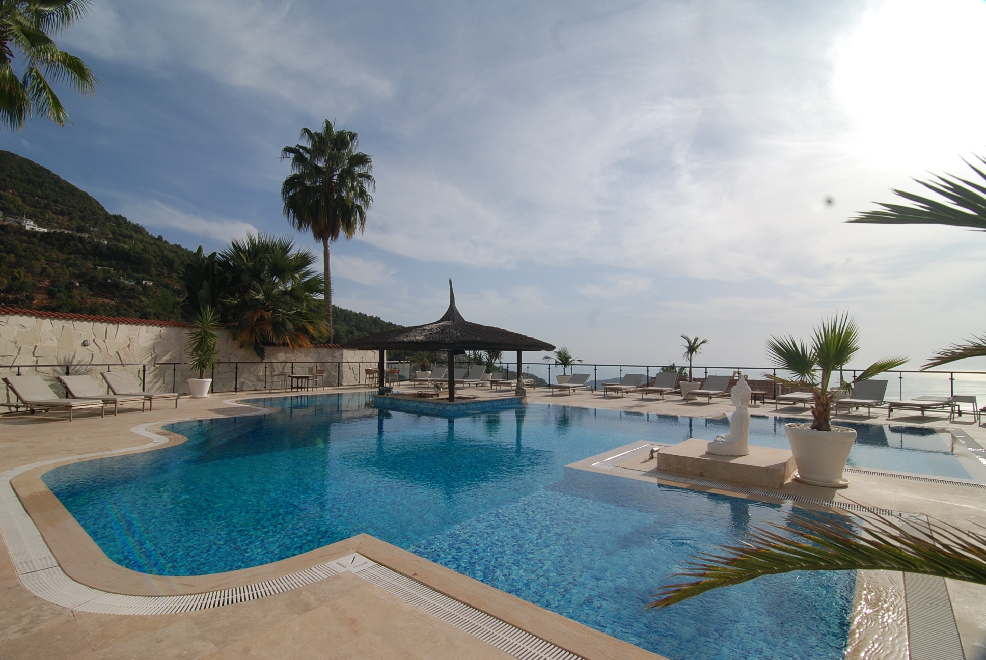 Open pool with loungers and thatched shades overlooking the sea in Alanya where homes are for sale