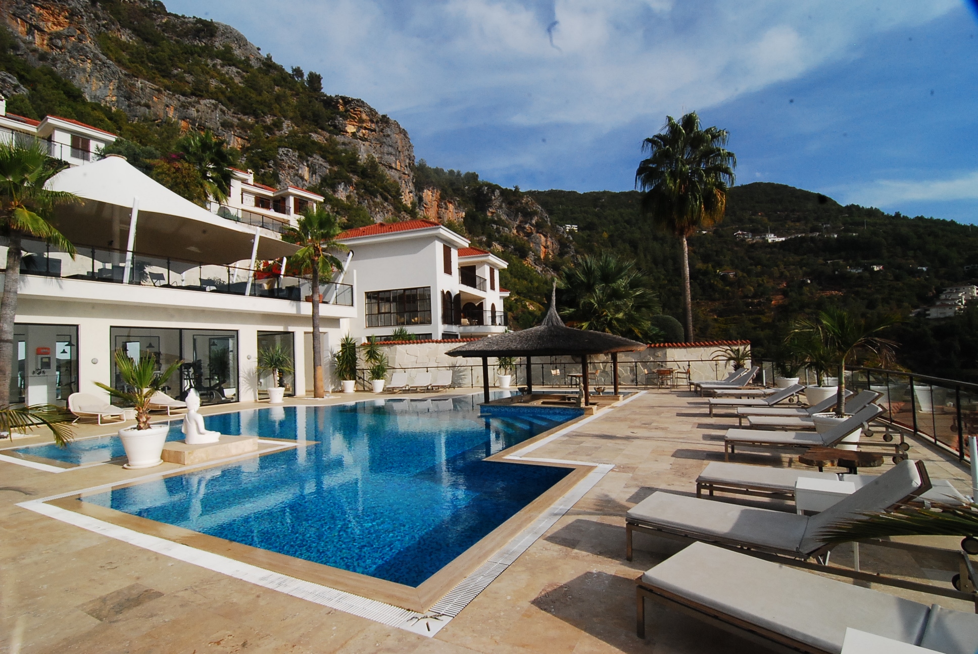 Large outdoor pool with loungers beside white villas and red roofs in an Alanya villa in Turkey