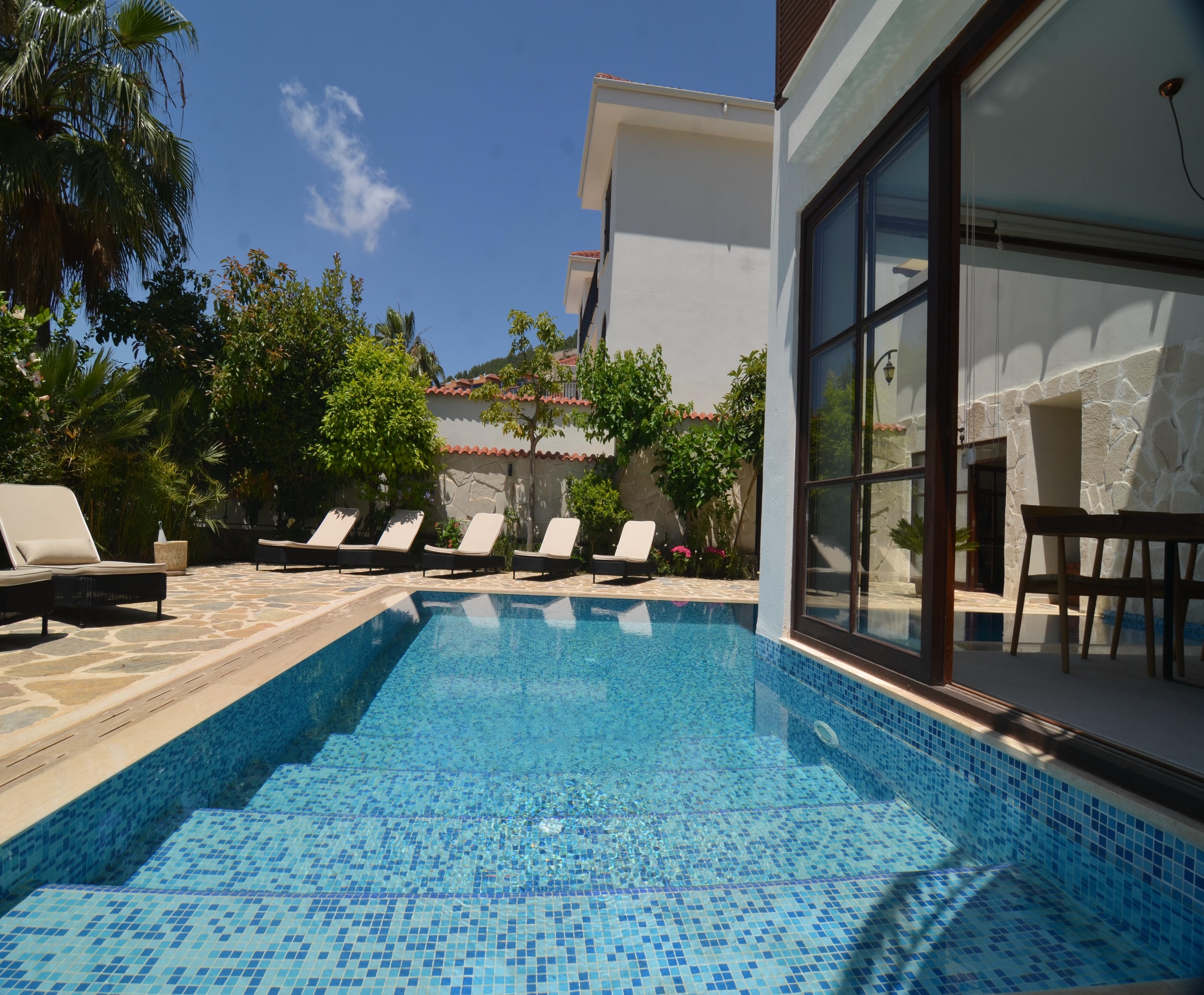 Private blue mosaic pool with loungers beside a villa facade and tropical plants in Turkey for sale