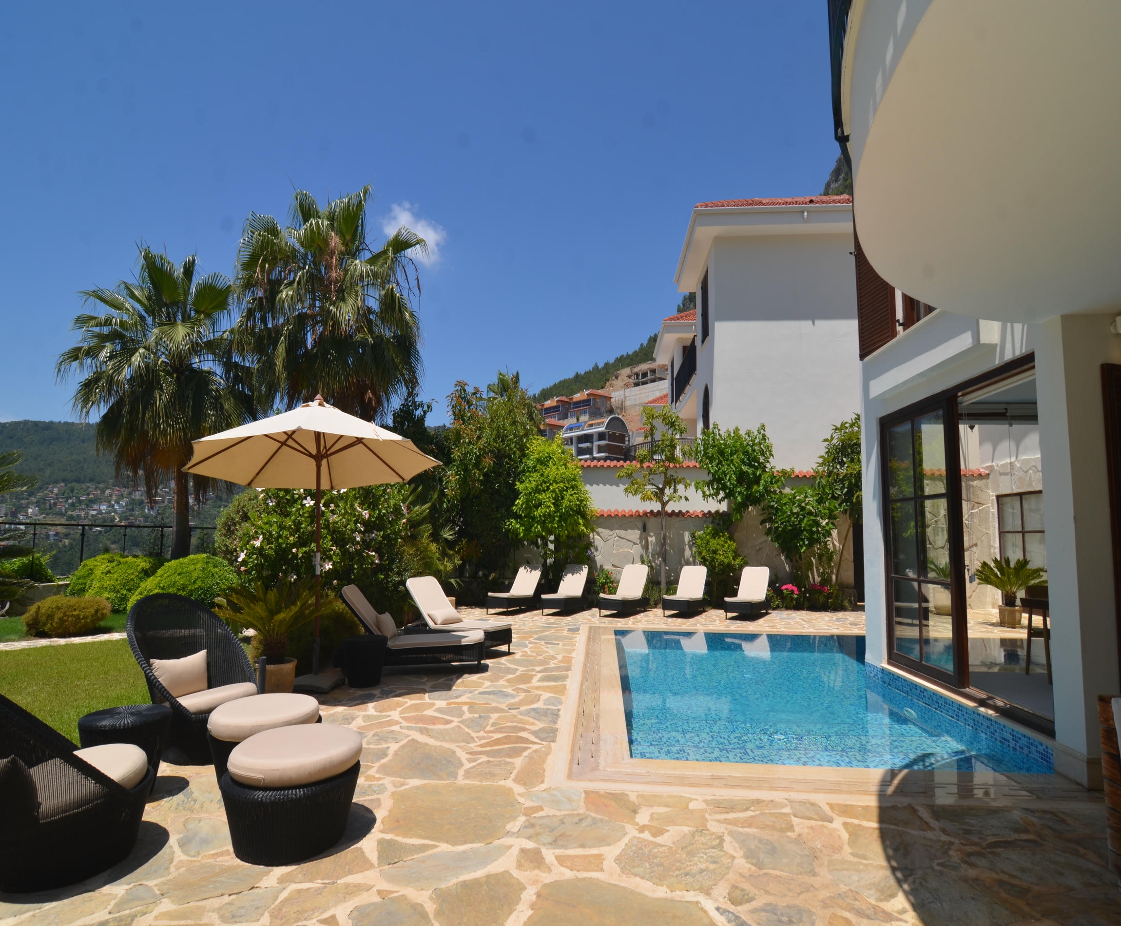 Courtyard pool with white loungers and wicker chairs overlooking mountain scenery in Alanya, Turkey