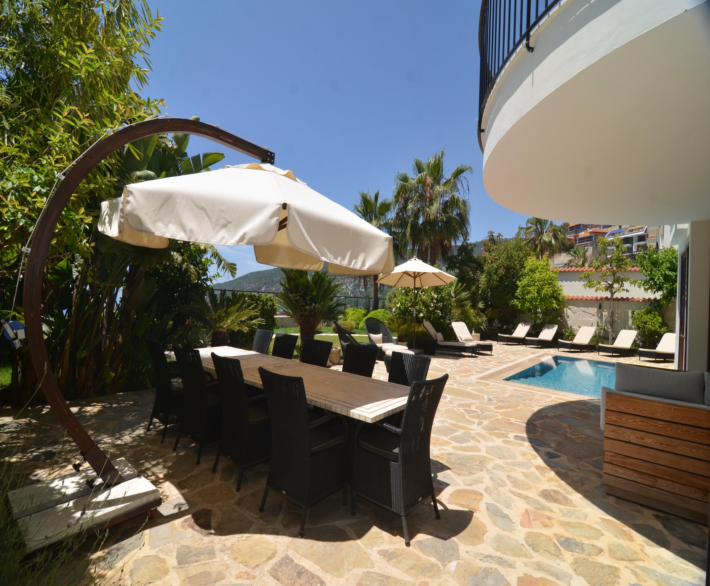 Dark wood dining table with wicker chairs beside a small pool and tropical plants at an Alanya villa