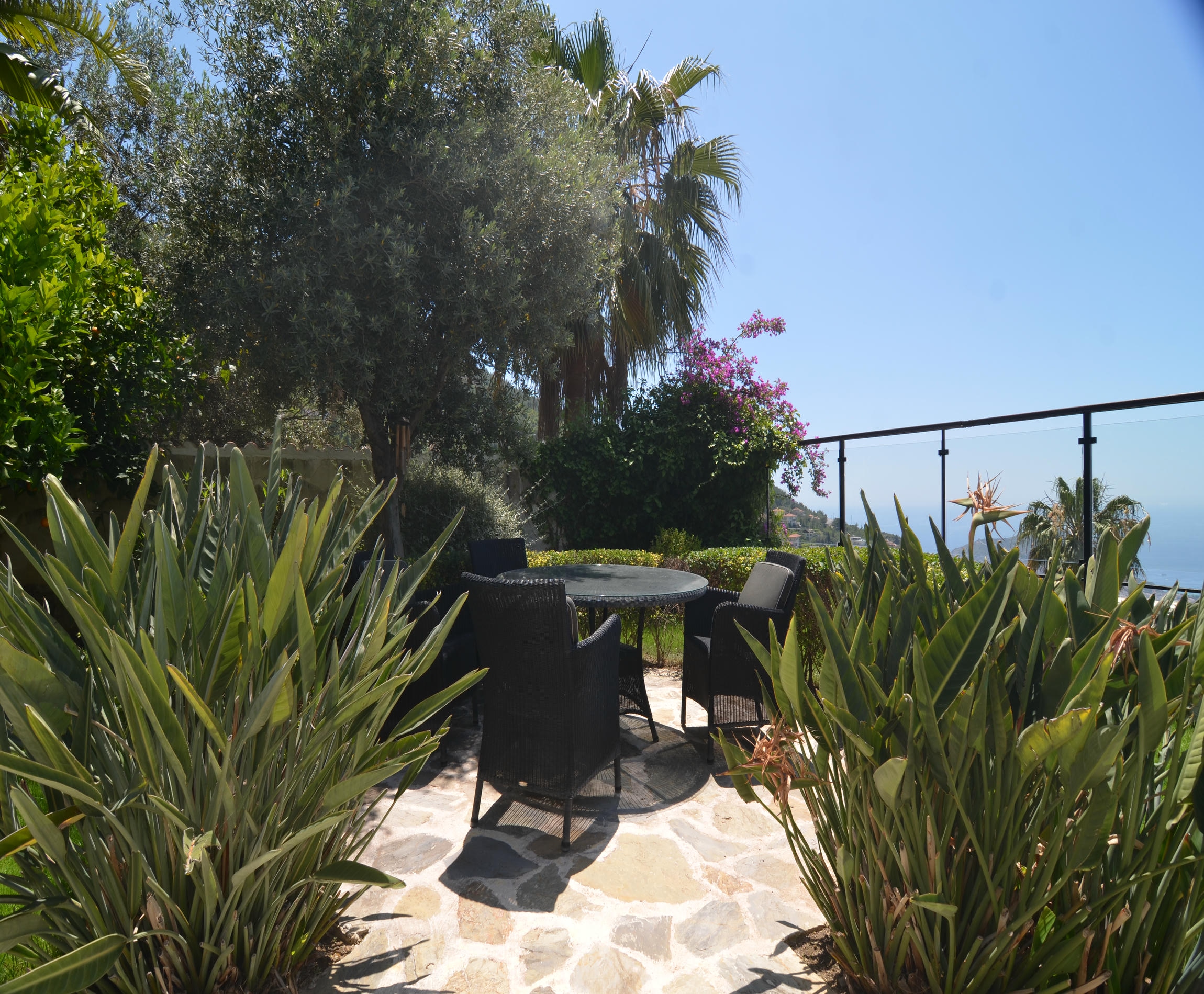 Stone terrace with a round table and four wicker chairs surrounded by palms in Alanya, Turkey