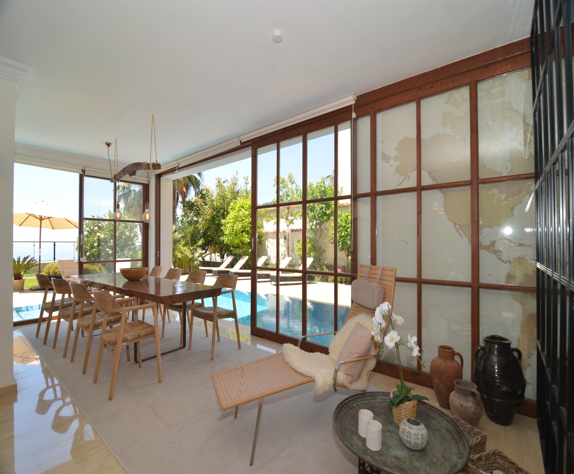 Dining room with a wooden table and pool behind the glass wall in Alanya where homes are for sale