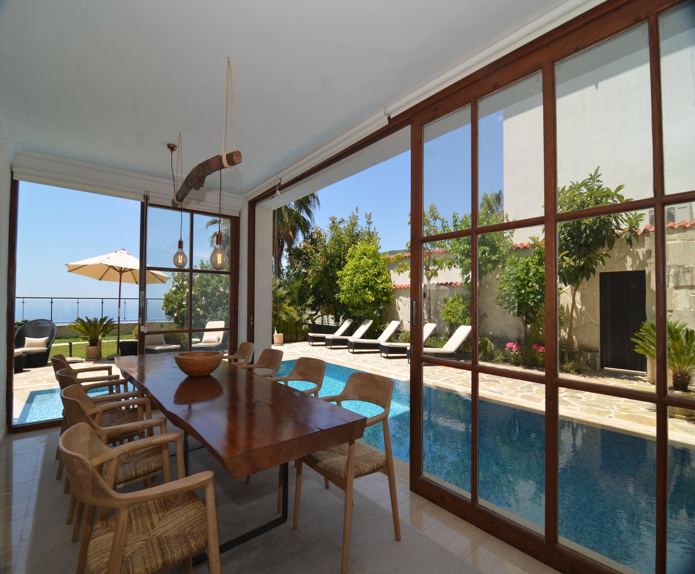 Dining room with panoramic glazing and an outdoor pool beyond the windows in a house for sale in Turkey