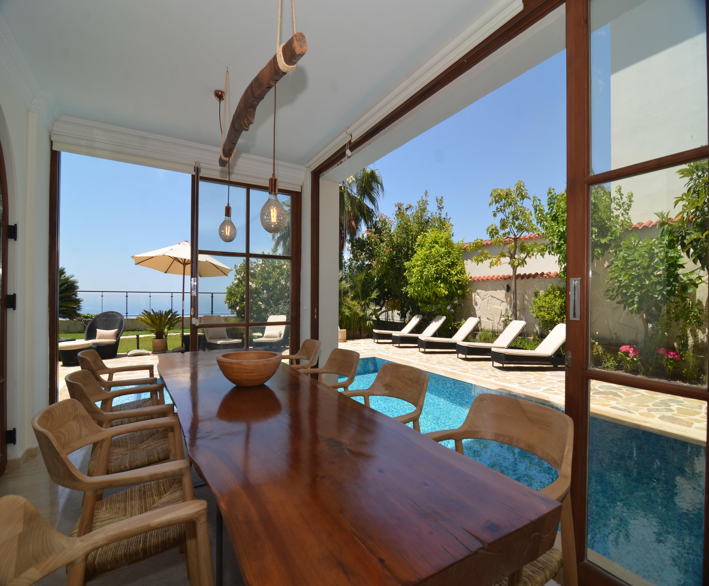 Dining room with a long wooden table and pool beside the room overlooking the sea in an Alanya villa for sale