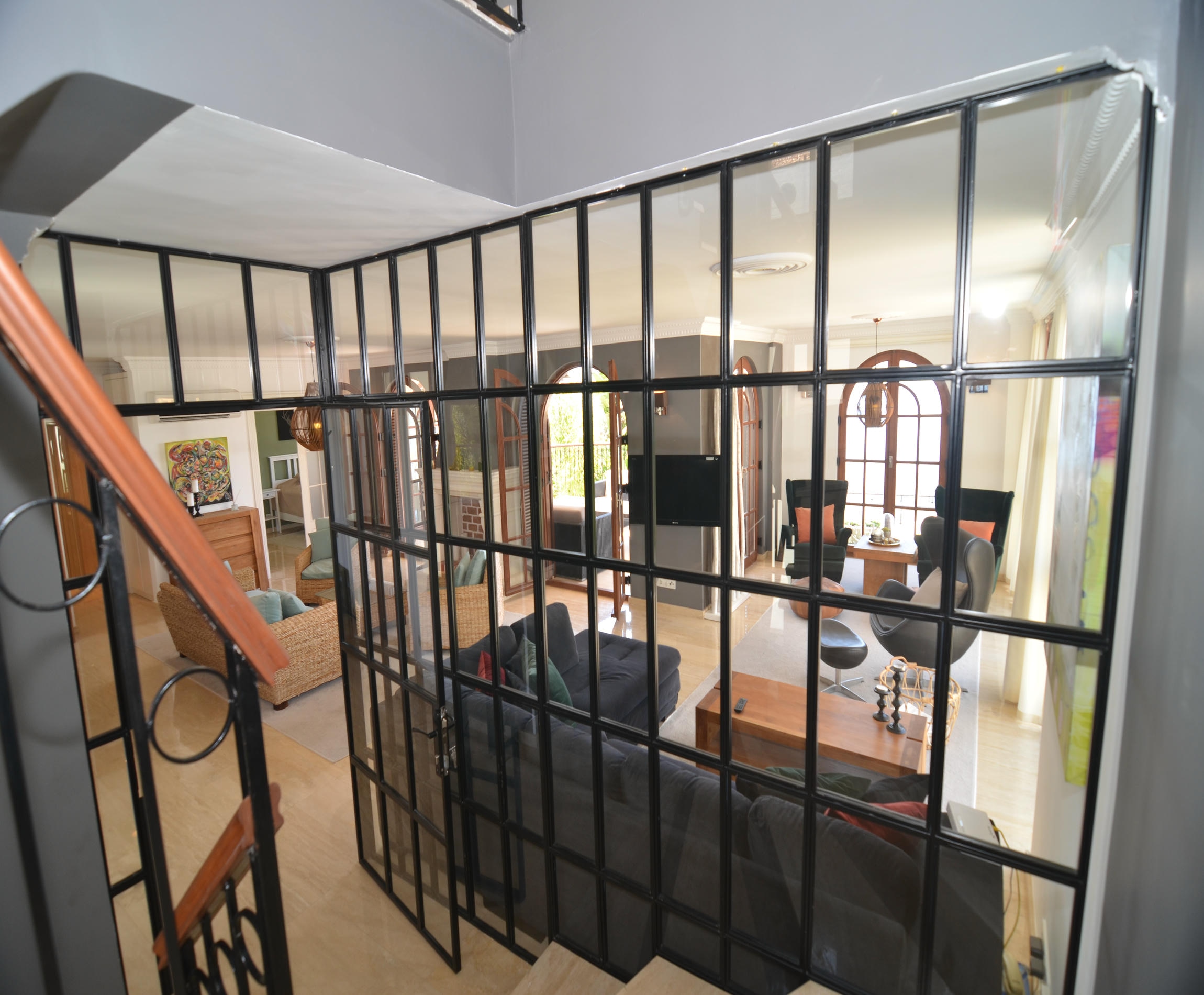 Hall with a wooden staircase, black glass partition and arched doorways in a villa